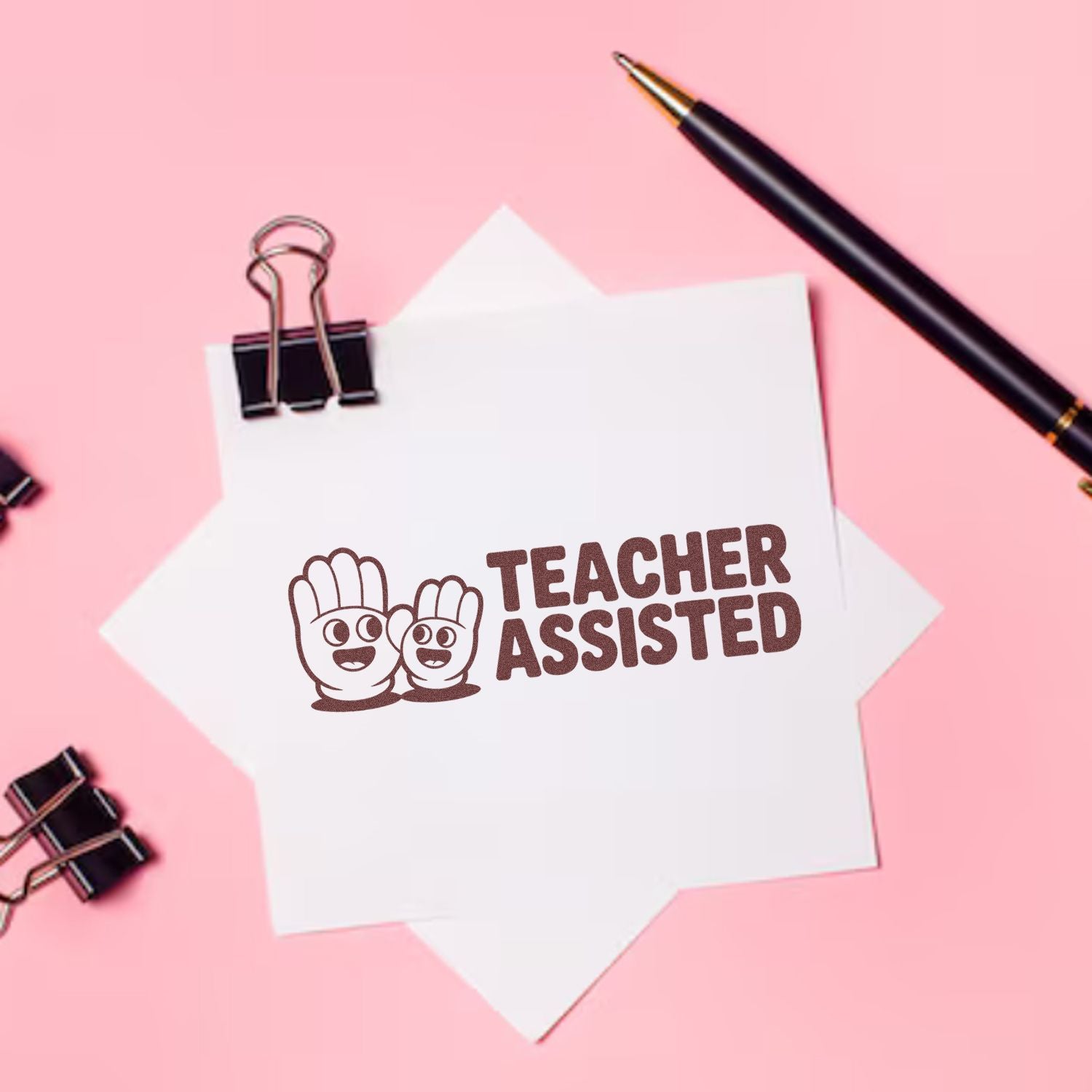Brown Teacher Assisted stamp seal on white paper, with black binder clips and pen on a pink background.