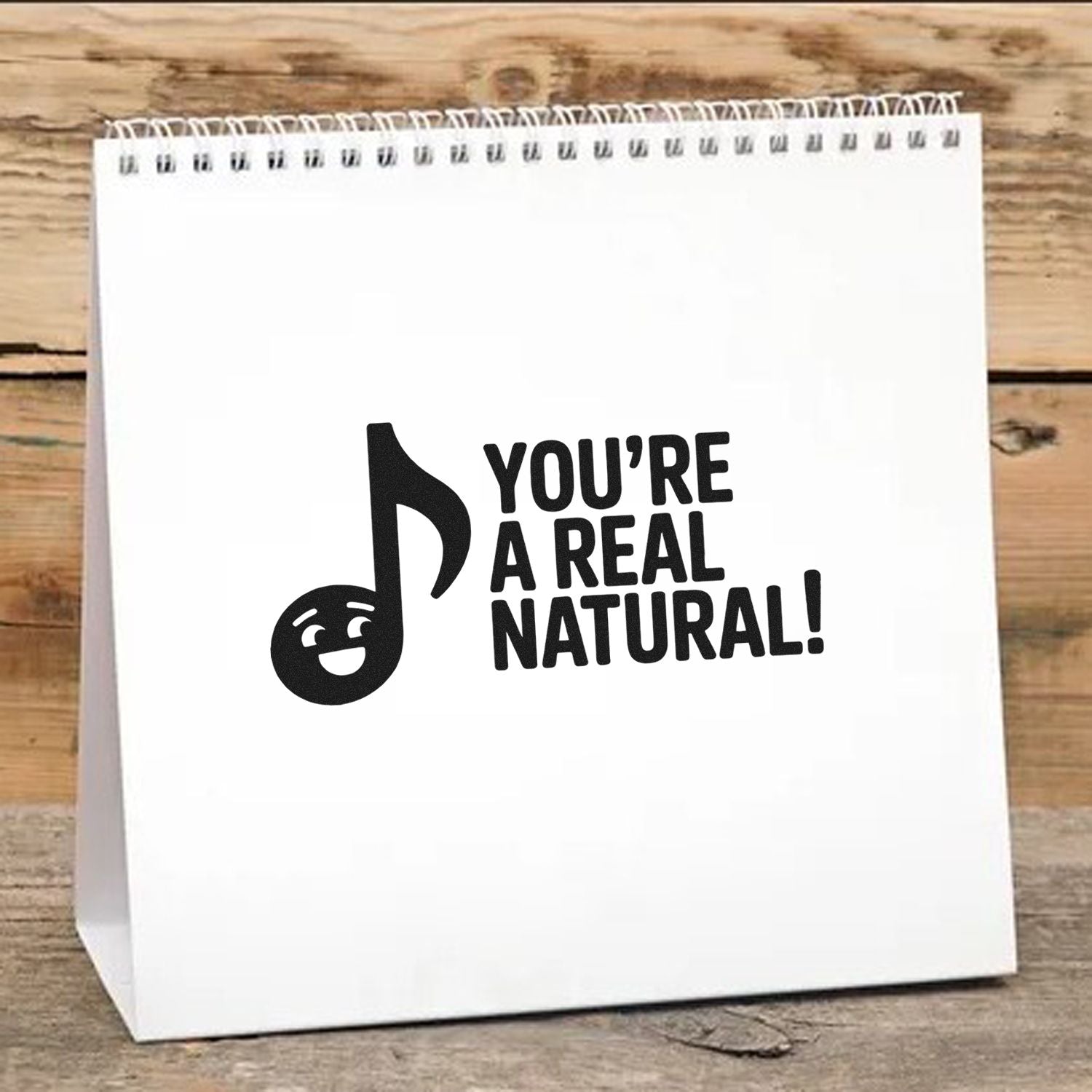 Black stamp and seal design with smiling music note and bold Youre a real natural! text on a white spiral-bound pad.