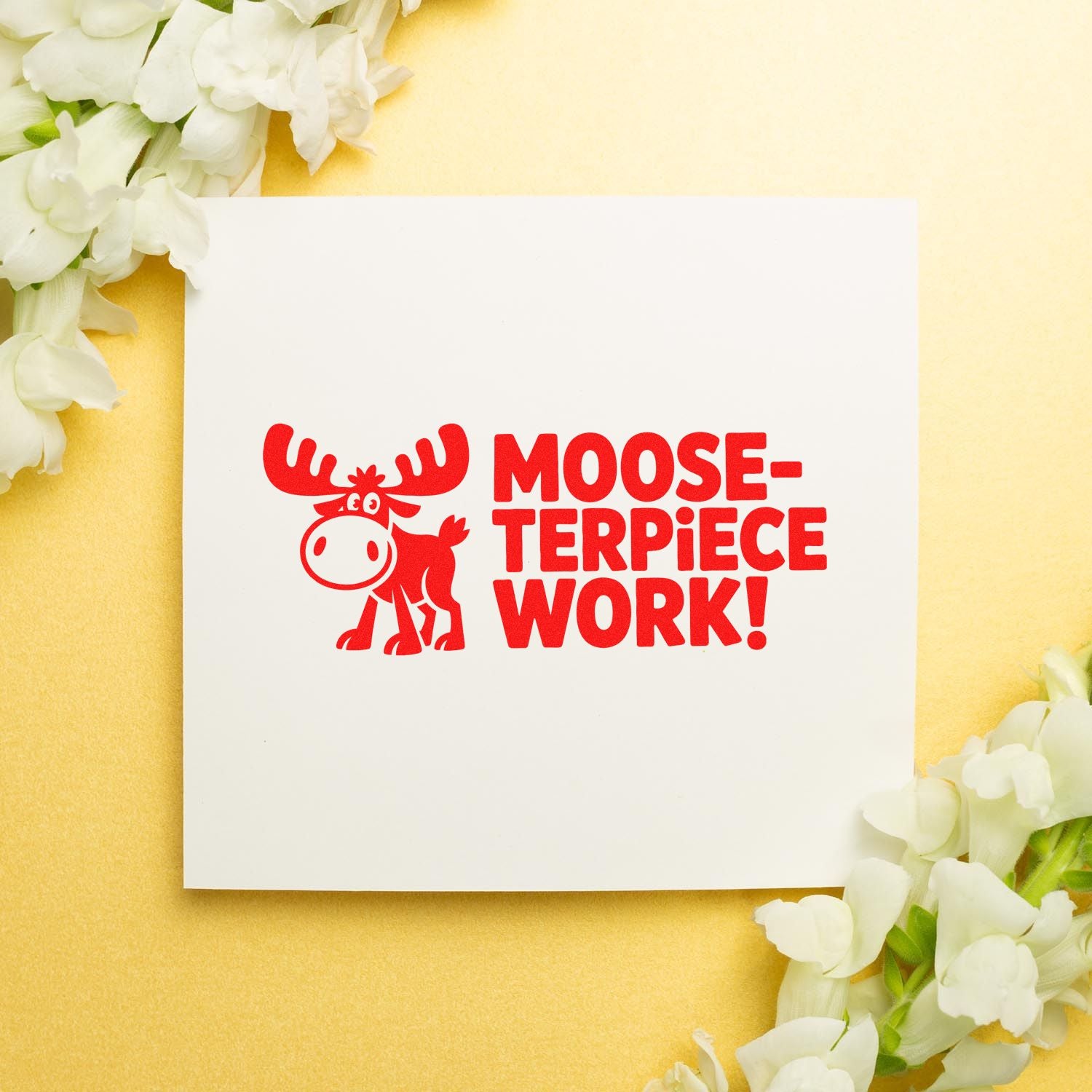 Red moose stamp and seal design reading Moose-terpiece Work! on a white card, with white flowers on a pale yellow background.
