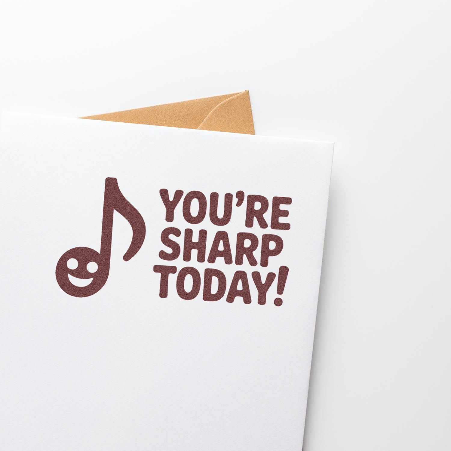 Brown stamp seal on a white envelope, reading YOURE SHARP TODAY! with a musical note smiley; tan envelope peeks behind.