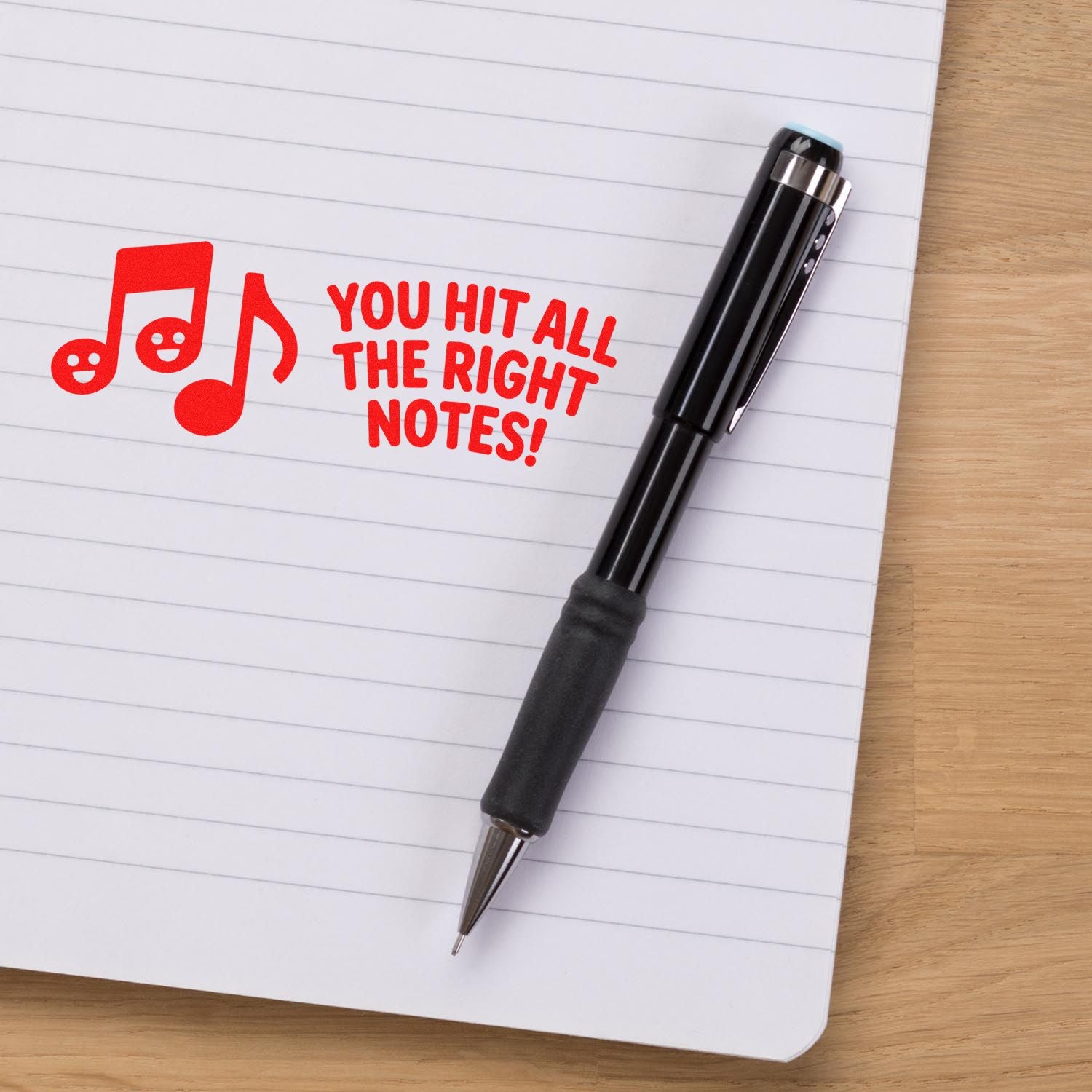 Black self-inking stamp pen on lined notebook, with red music notes and You Hit All the Right Notes! seal.