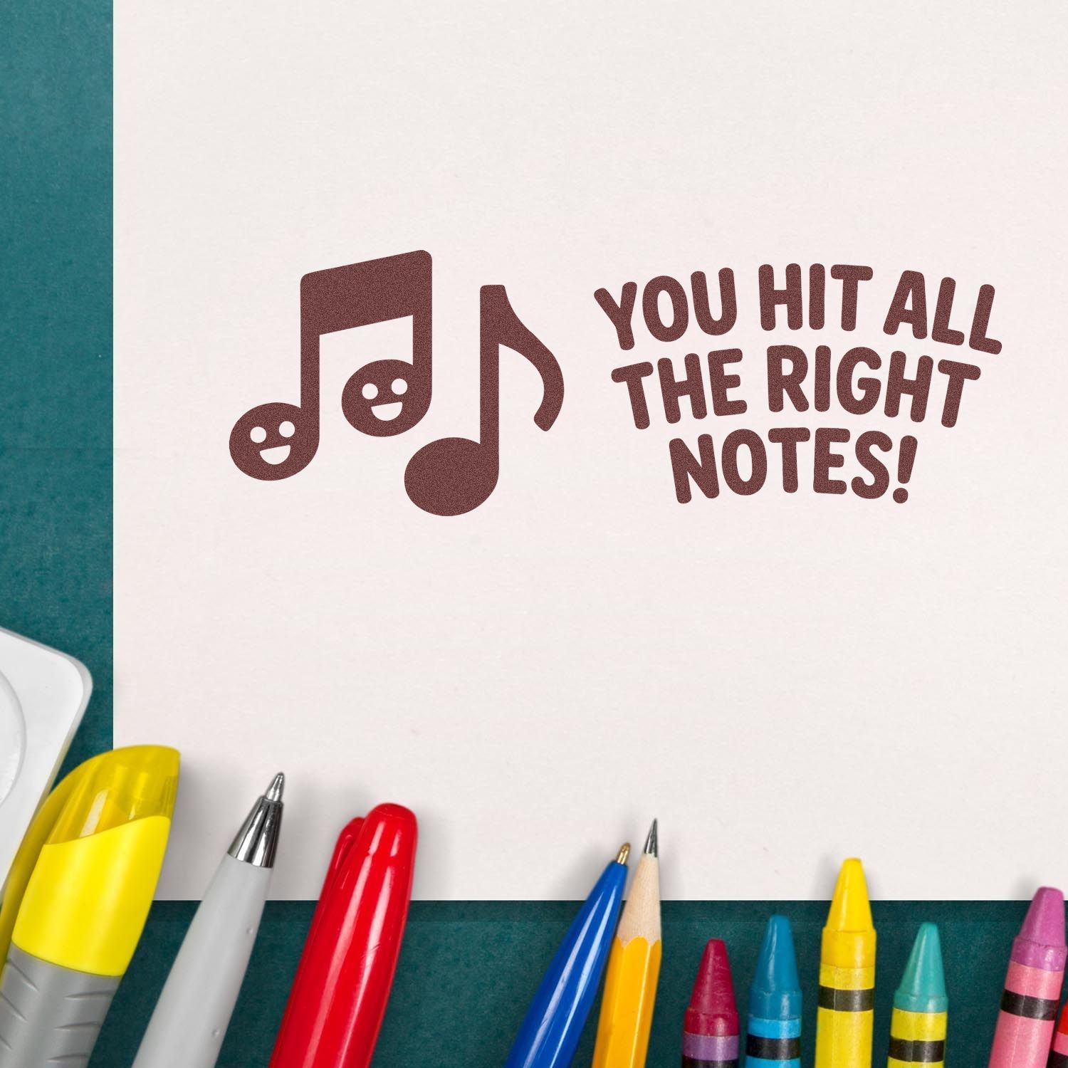 Brown music note stamp seal reading You hit all the right notes! on white paper, with colorful pens and markers around it.