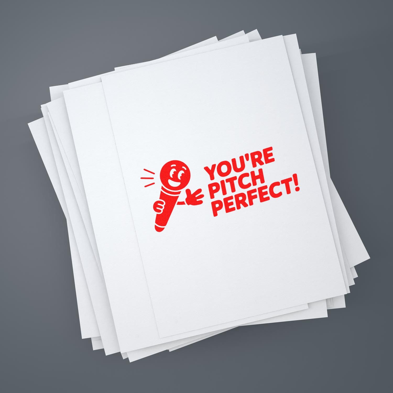 Red rubber stamp reading Youre pitch perfect! on stacked white papers, with a red microphone mascot.