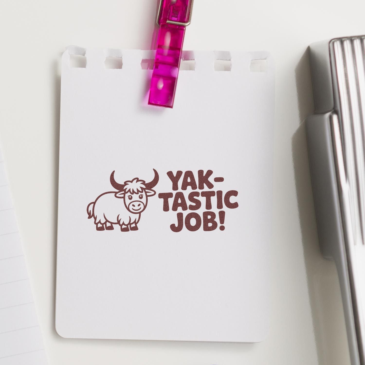 Brown yak stamp with YAK-TASTIC JOB! on white paper, clipped with a pink clip beside a silver seal tool.
