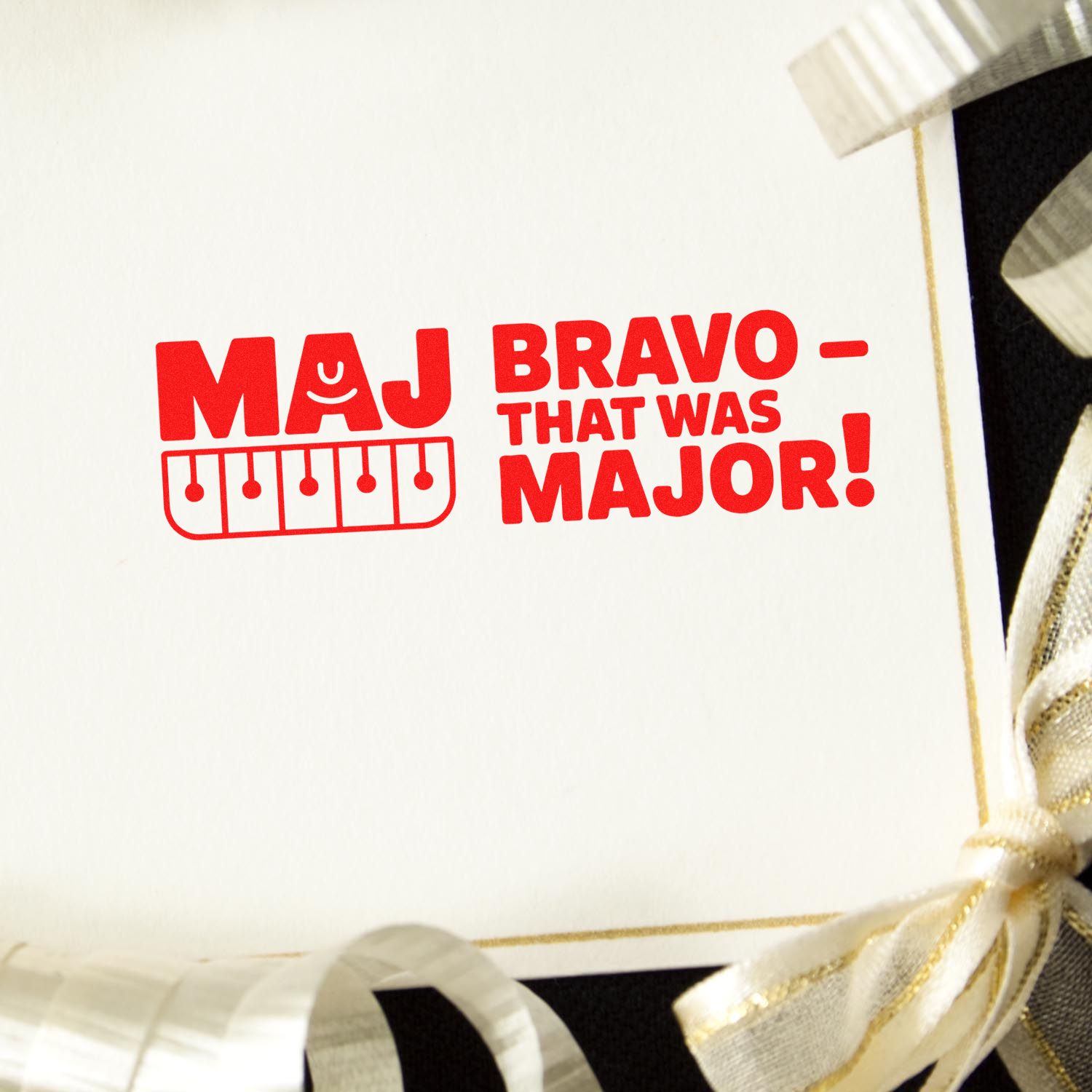 Red MAJ BRAVO stamp seal on white card with gold ribbon, featuring That Was Major! and piano keys.