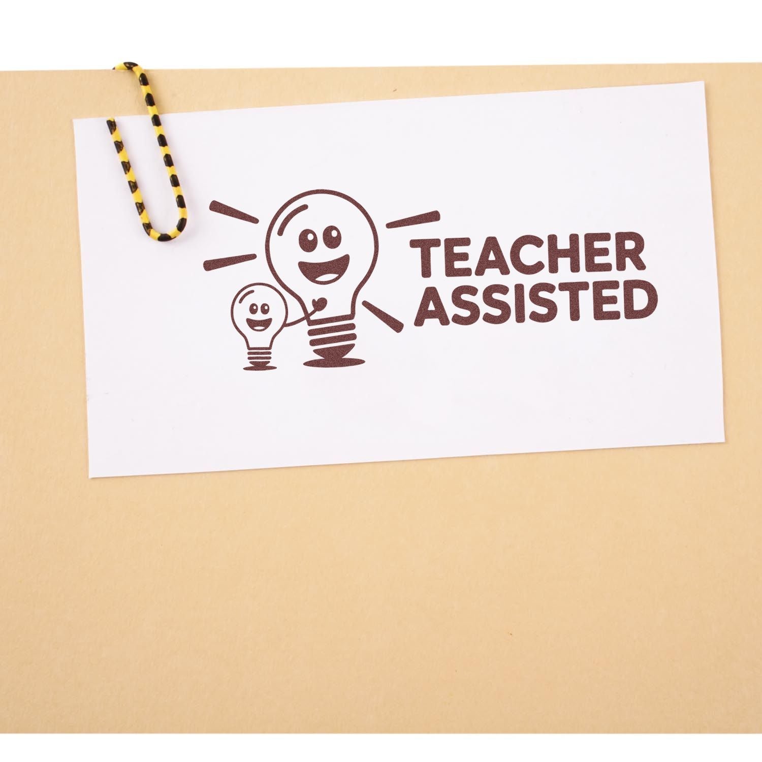 Teacher Assisted brown stamp with smiling lightbulb icons on white paper, clipped with yellow-black paperclip on tan background.