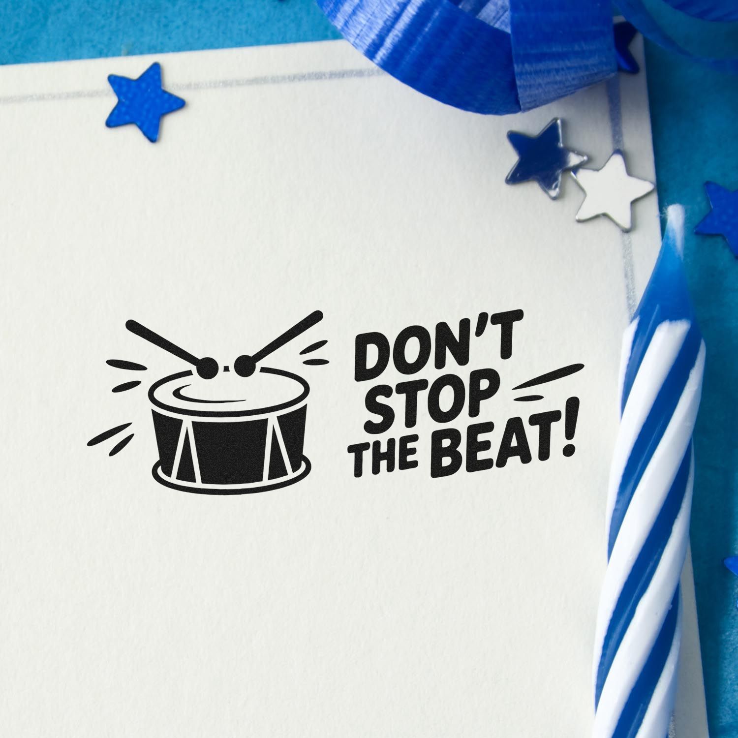 Black drum stamp and seal with DONT STOP THE BEAT! on white card, accented by blue ribbon, stars, and confetti.