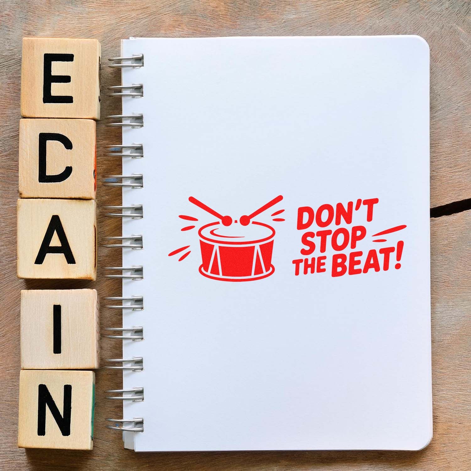 Wooden letter stamp blocks and a red drum seal on a white spiral notebook reading Dont Stop the Beat!