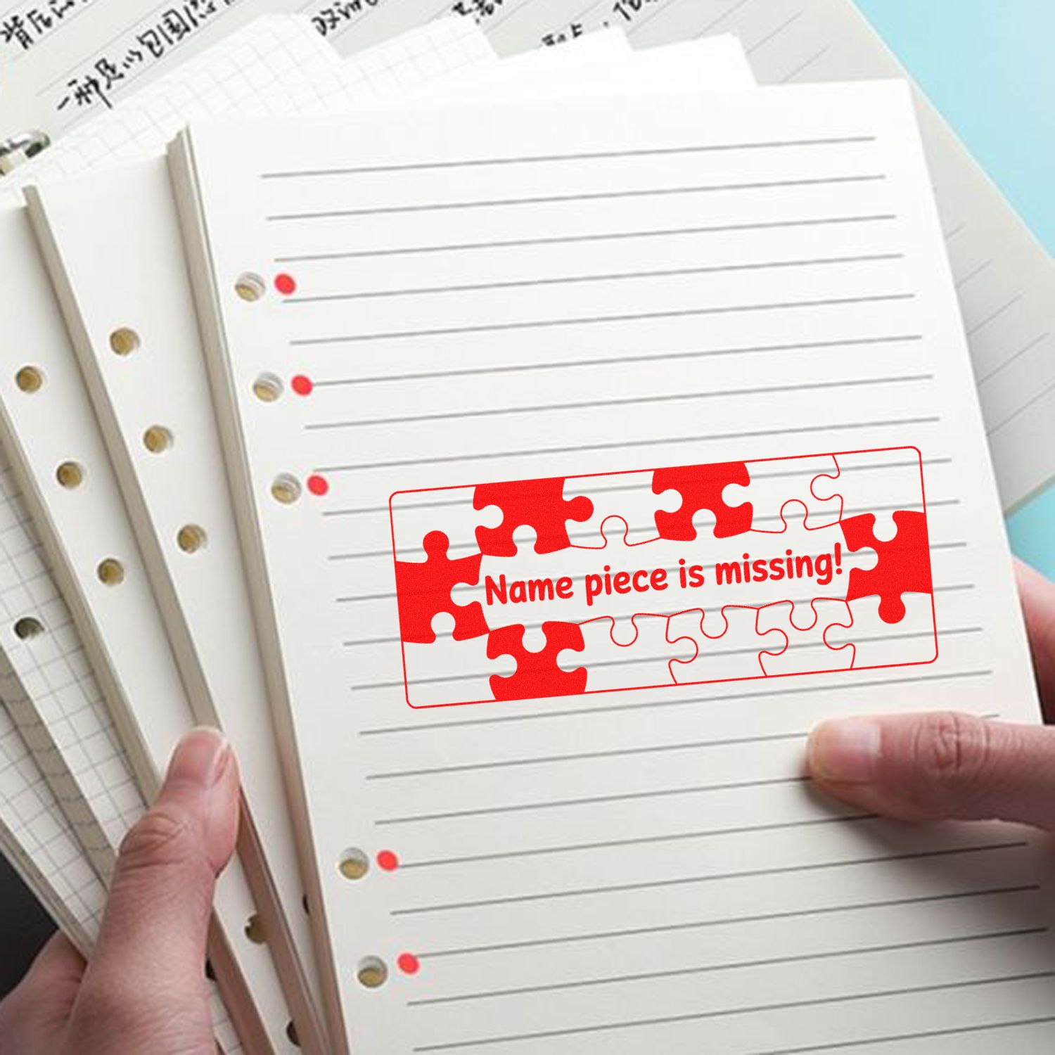 Red puzzle-piece name seal stamp on lined notebook pages held by hands