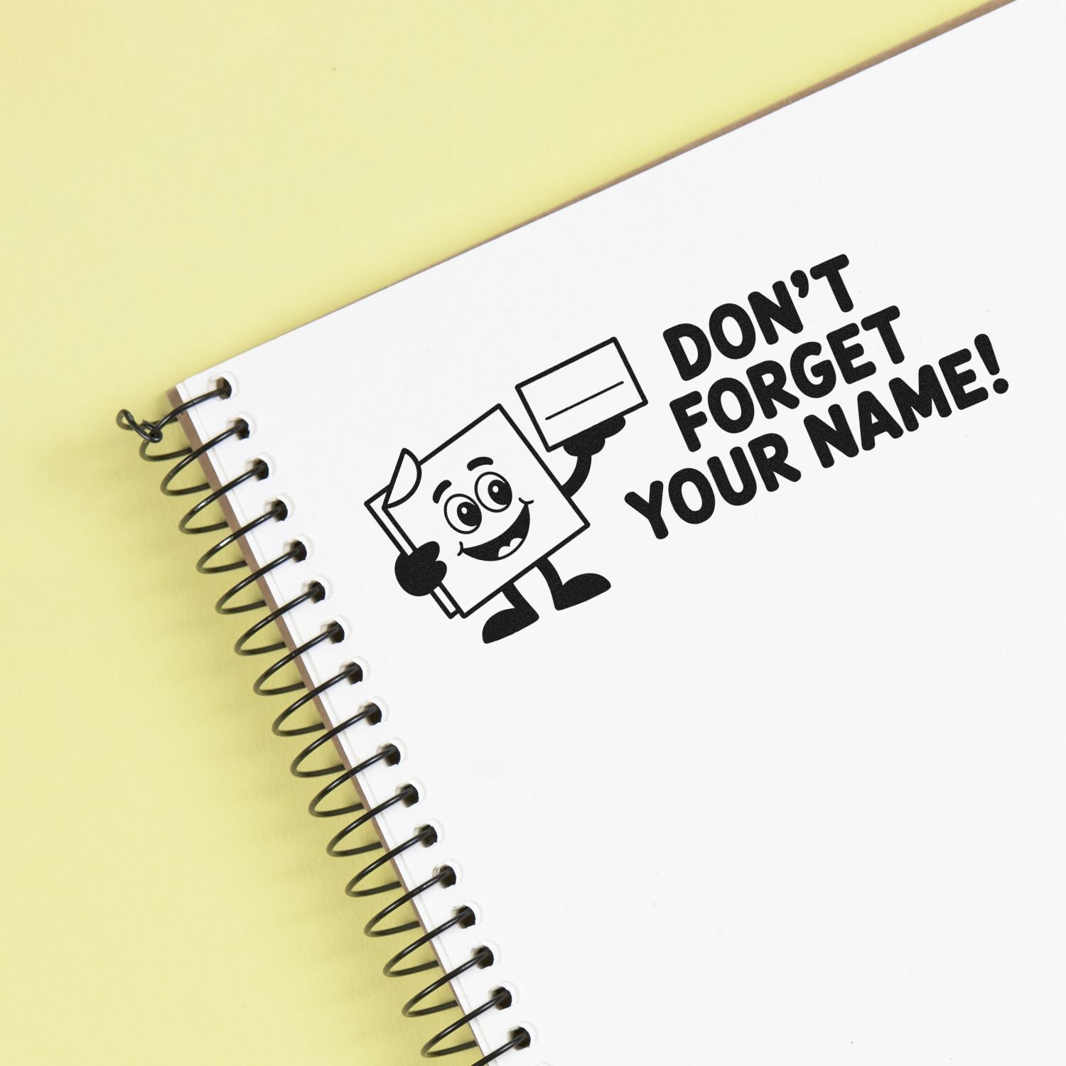Custom stamp and seal design on white spiral notebook with black Dont forget your name! text, on pale yellow background.