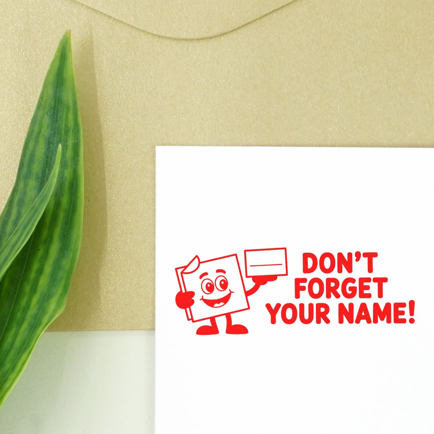 Red self-inking stamp design with cartoon and DONT FORGET YOUR NAME! on white, beside a green leaf on beige.