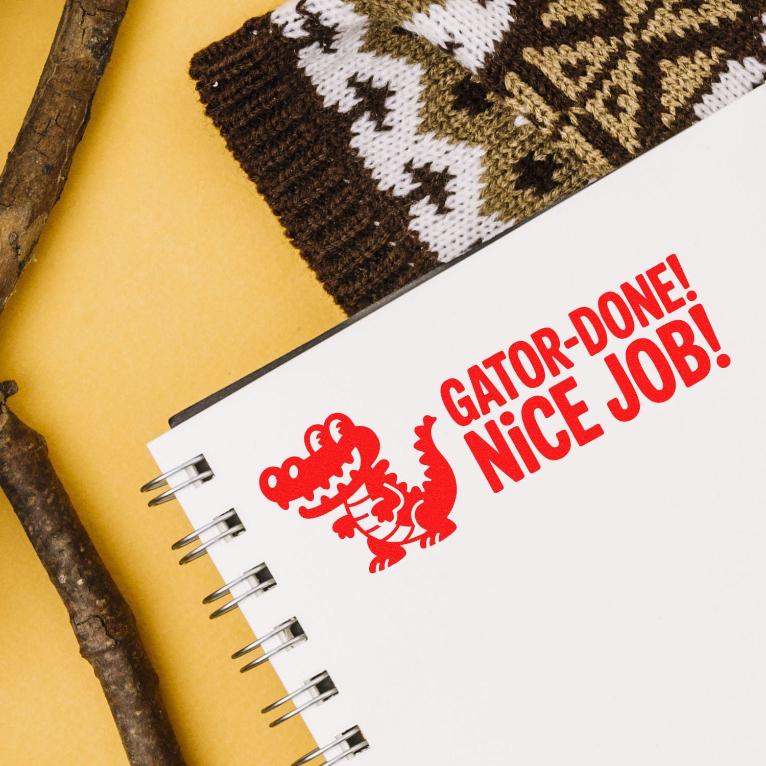Red crocodile stamp and seal on white spiral notebook reading GATOR-DONE! NICE JOB! against yellow with brown knit.