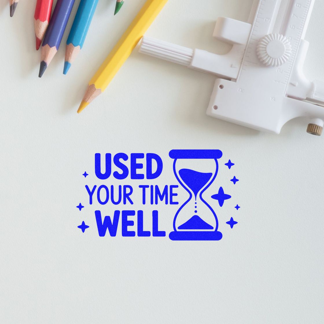 Blue rubber stamp seal imprint with hourglass and Used your time well, beside a white stamping tool and colored pencils.