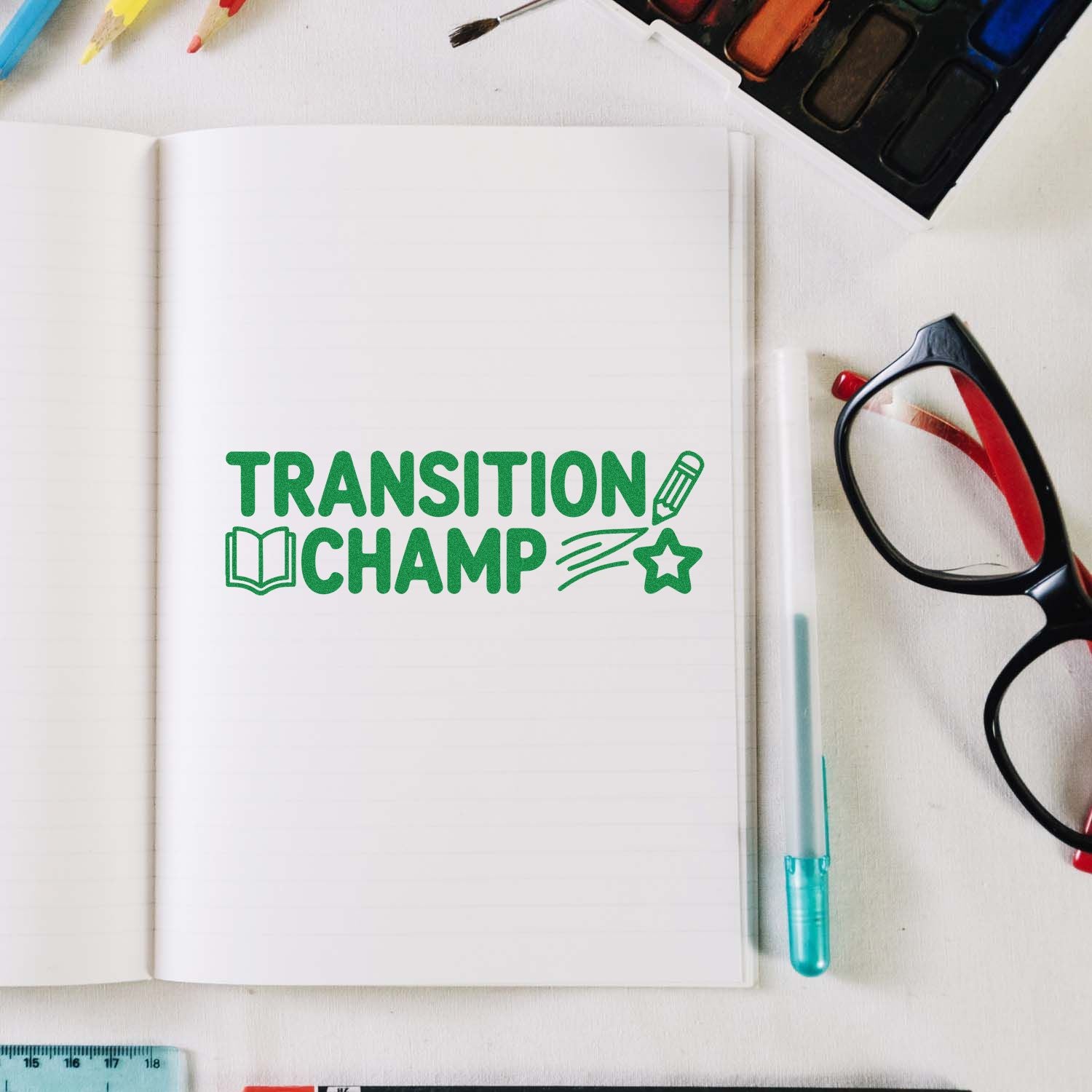 Green Transition Champ stamp seal on open notebook, with book, pencil and star icons; black glasses and turquoise pen nearby.