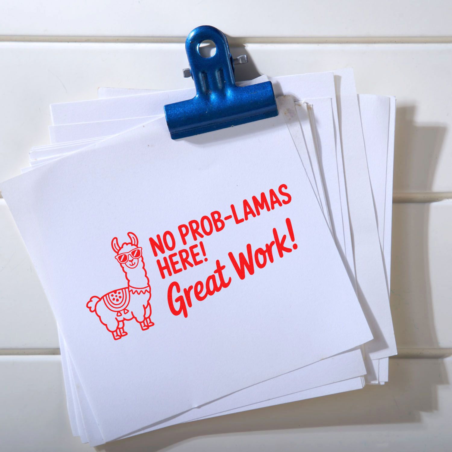 Blue binder clip holding white papers with a red custom stamp seal: llama and No Prob-Lamas Here! Great Work!