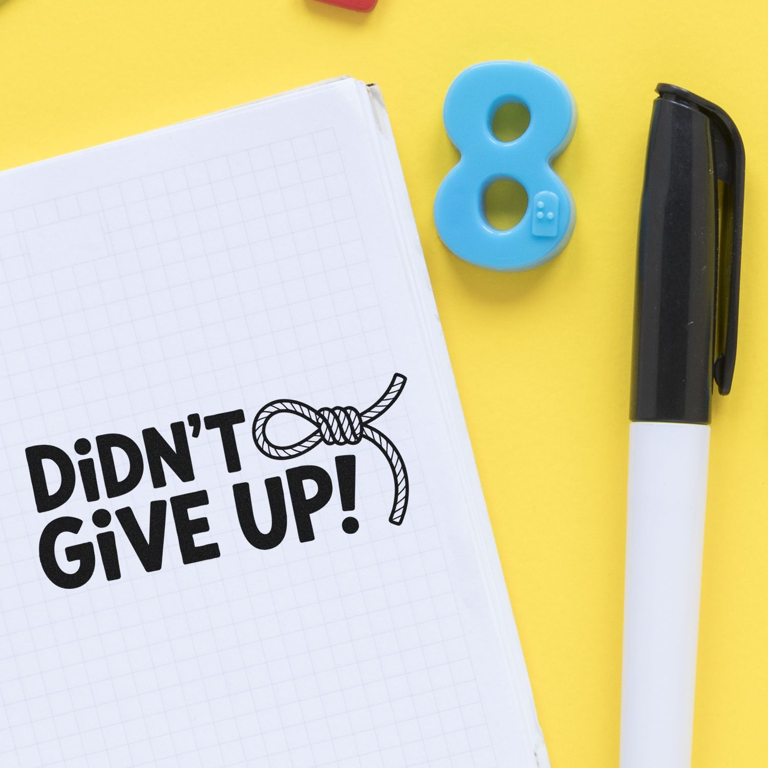 Notebook with DIDNT GIVE UP! stamp, blue number 8 seal, and black marker on a yellow background.