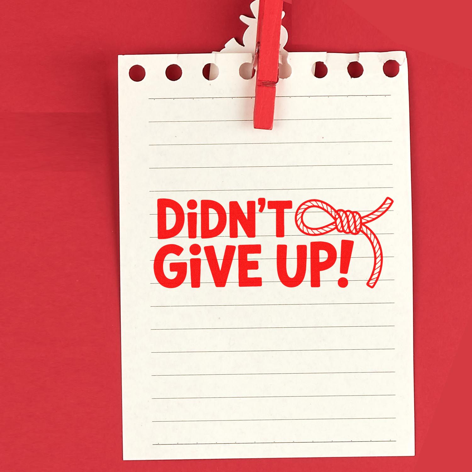 Red seal stamp on white lined paper clipped with a red clothespin, reading DIDNT GIVE UP! with rope loop graphic.