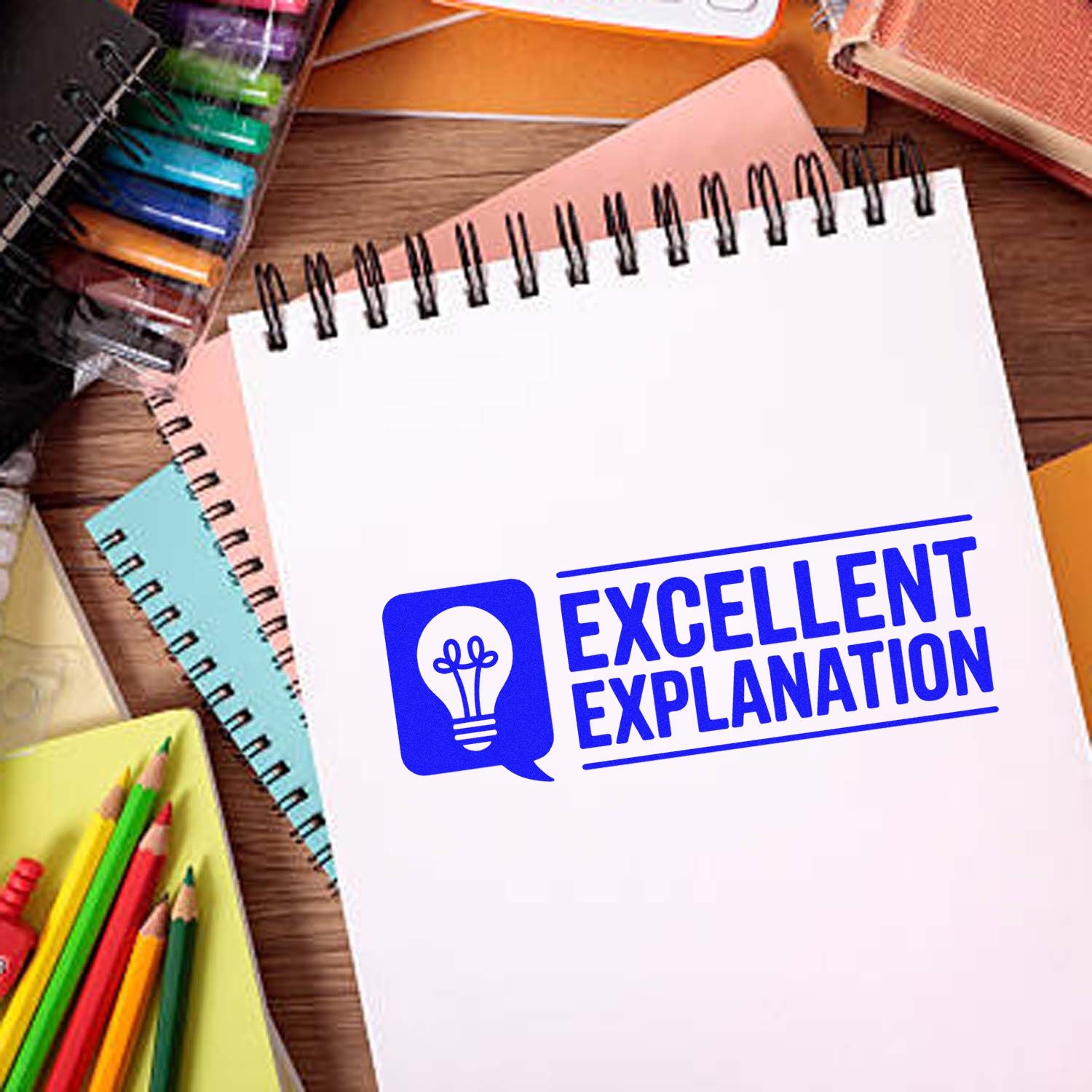 Blue Excellent Explanation stamp seal on a white spiral notebook, with colorful stationery on a wooden desk.
