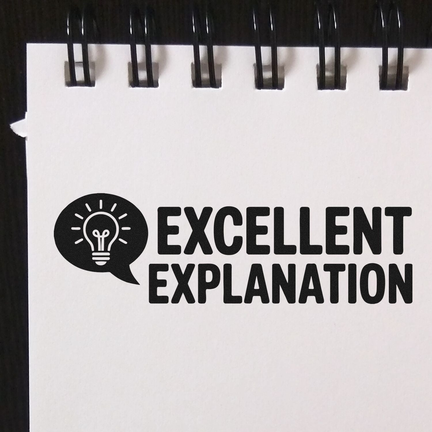 Black Excellent Explanation stamp seal with lightbulb icon on a white spiral-bound page