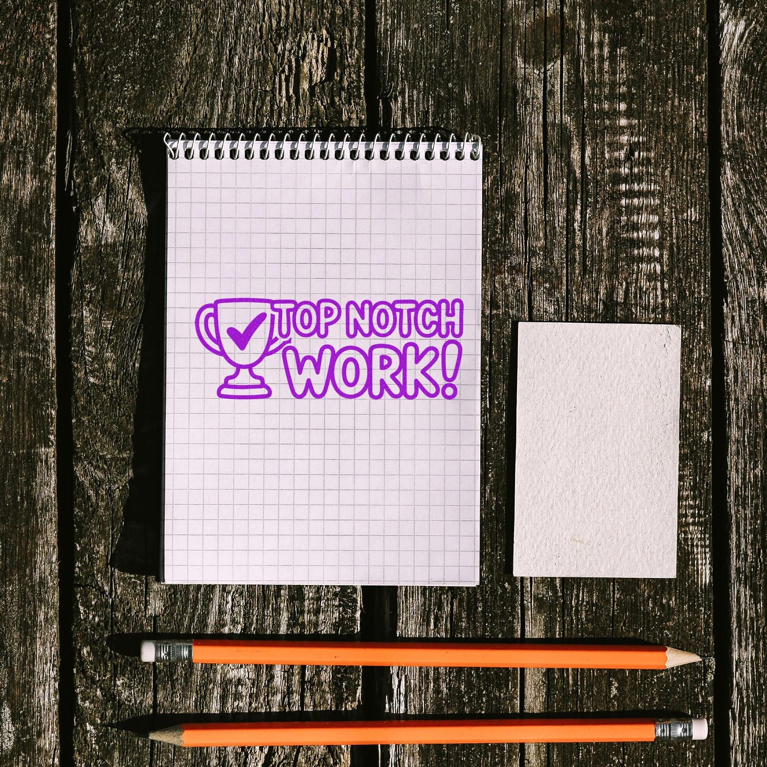 Purple Top Notch Work! stamp seal on graph notebook, with blank card and two orange pencils on rustic wood.
