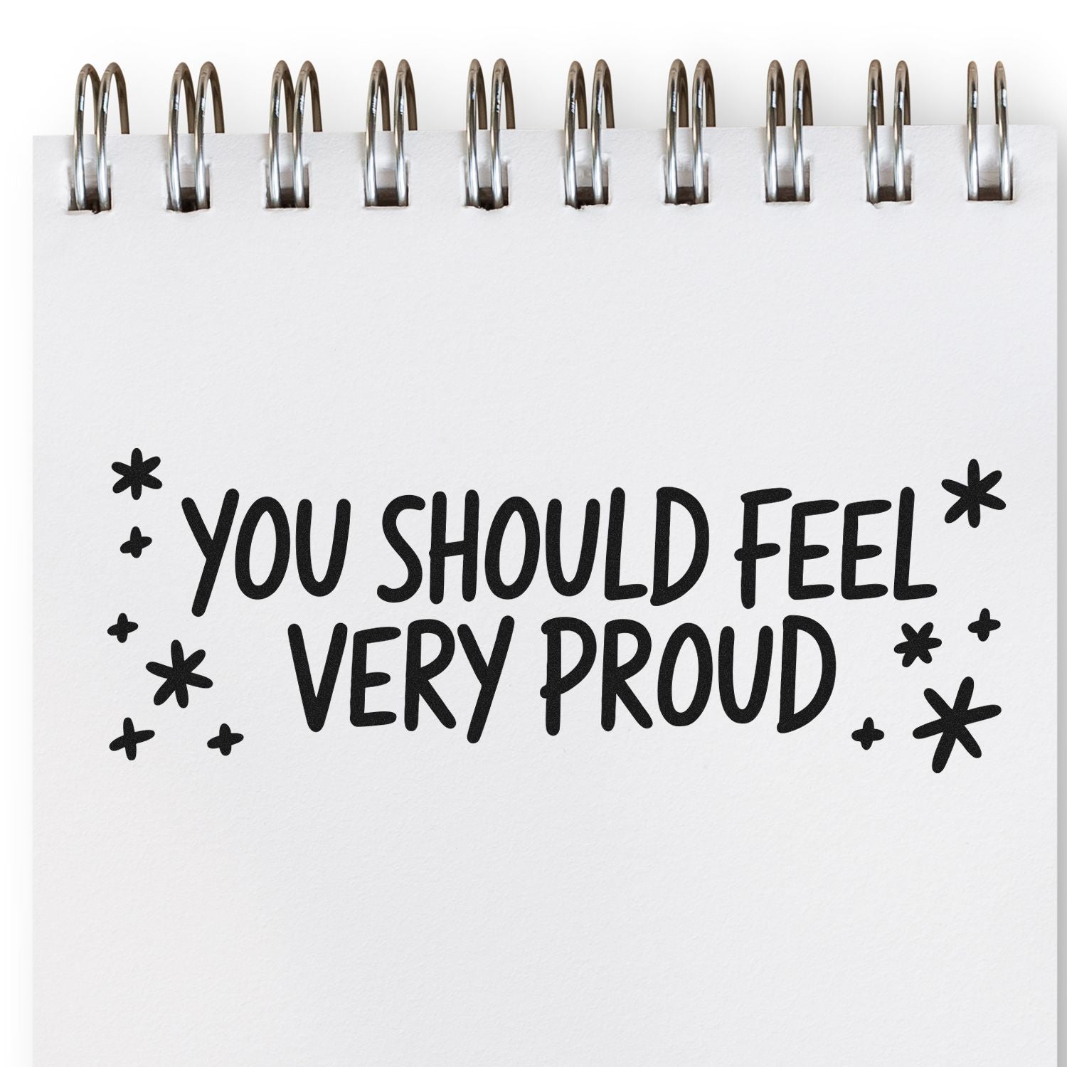 Black motivational stamp and seal reading You should feel very proud with asterisks on a white spiral notebook page.