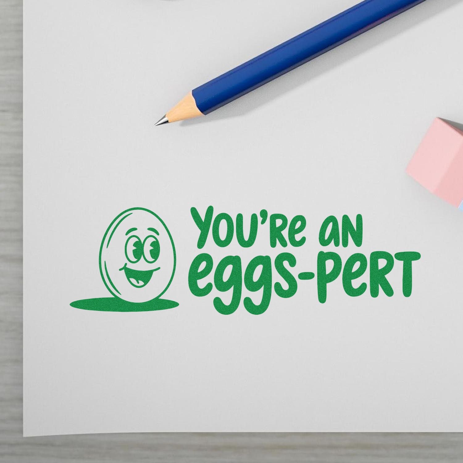 Green stamp and seal reading Youre an eggs-pert with a smiling egg icon, plus a blue pencil and pink note.