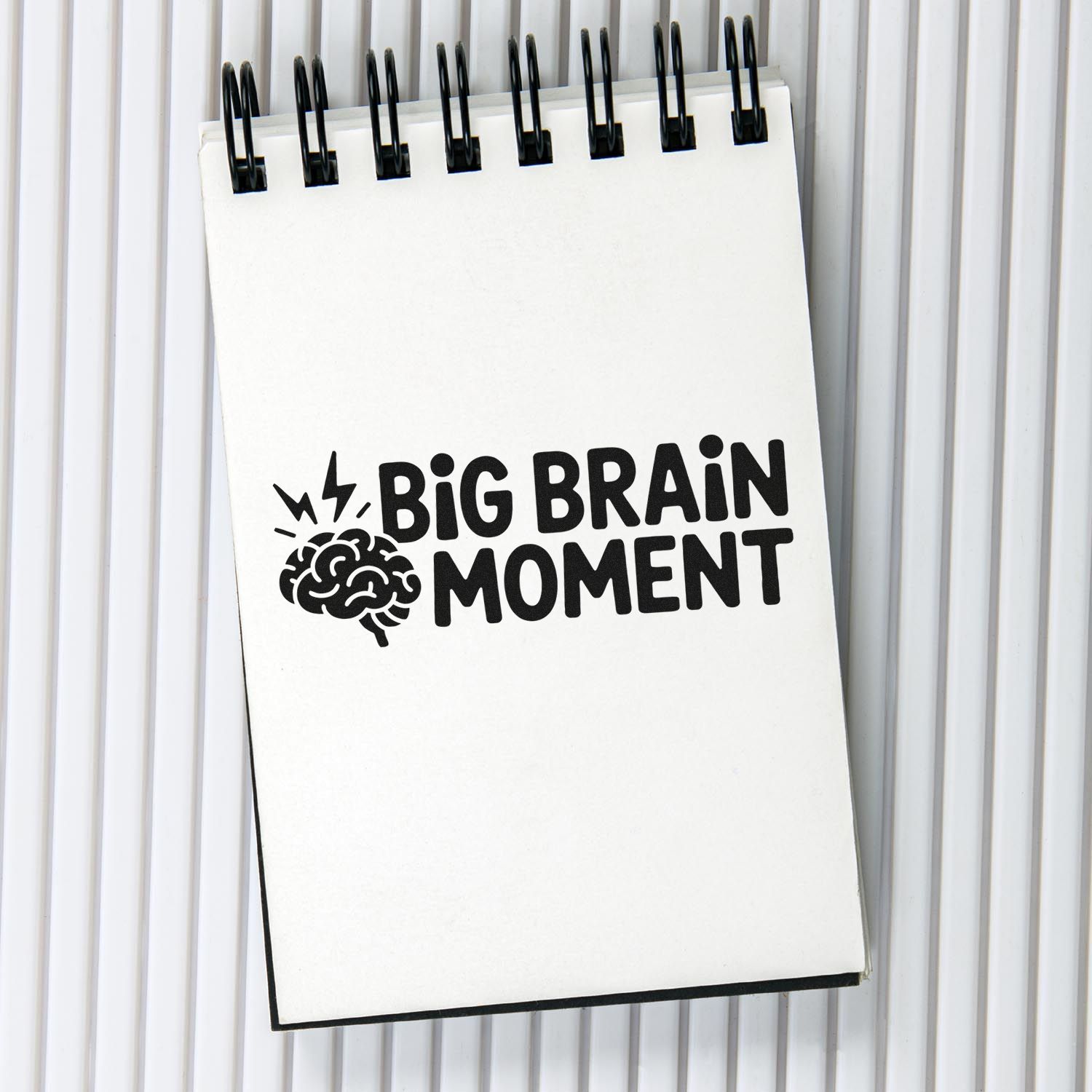 Black stamp and seal design on a white spiral notepad reading Big Brain Moment with a brain icon.