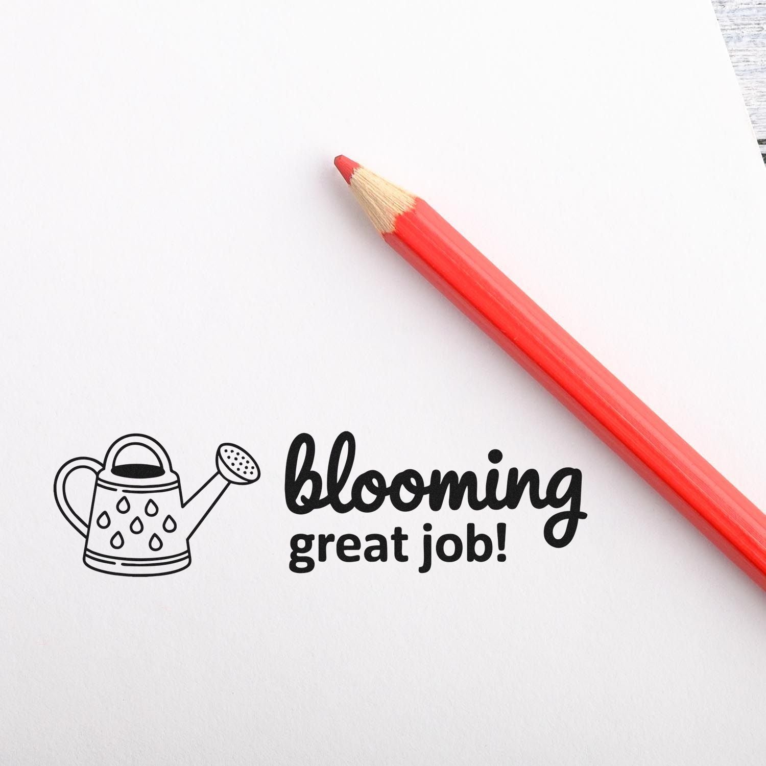 Black gardening stamp seal with watering can and blooming great job! text beside a red pencil on white paper.