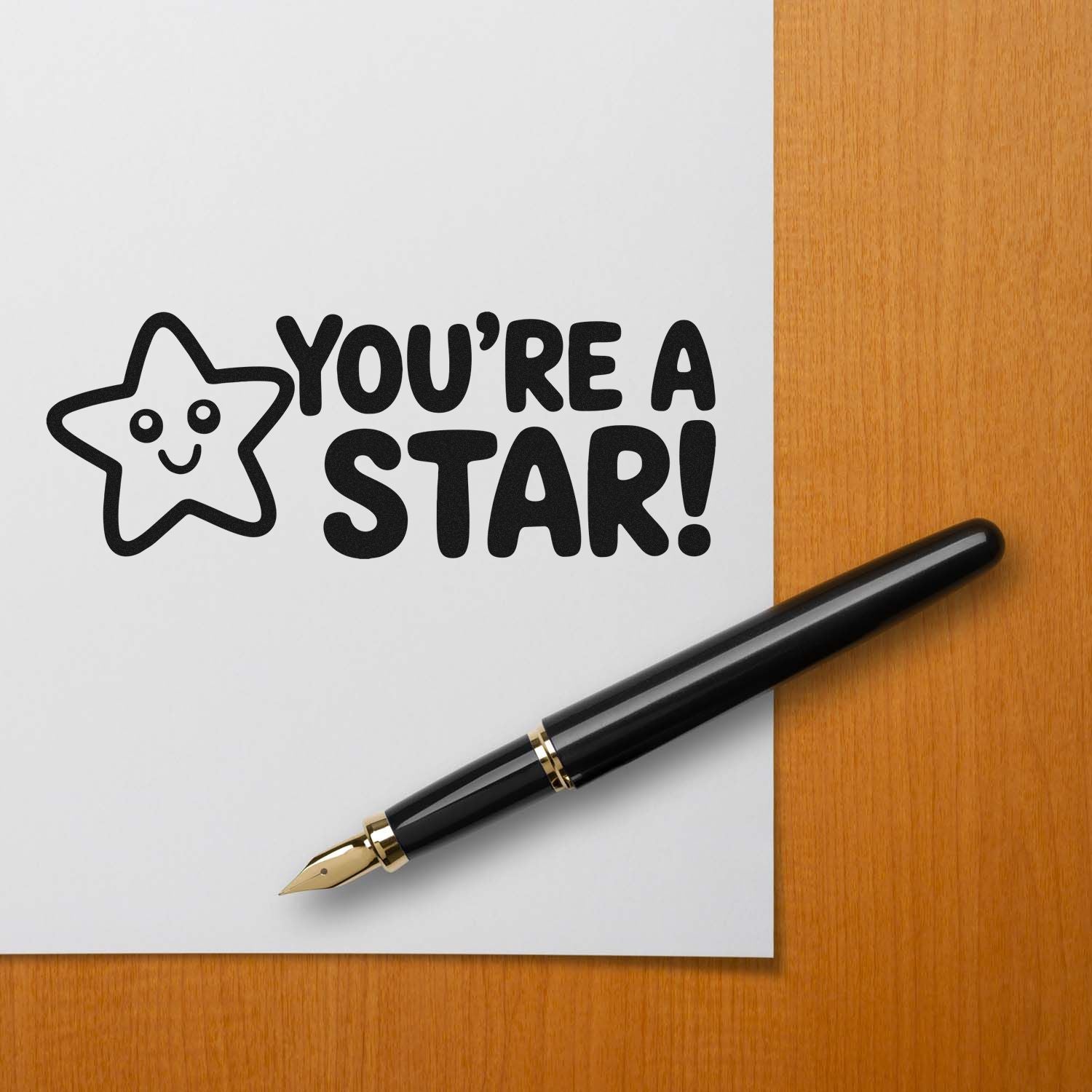 Black custom stamp/seal with smiling star and Youre a star! on white paper beside a gold-nib fountain pen on wood desk.