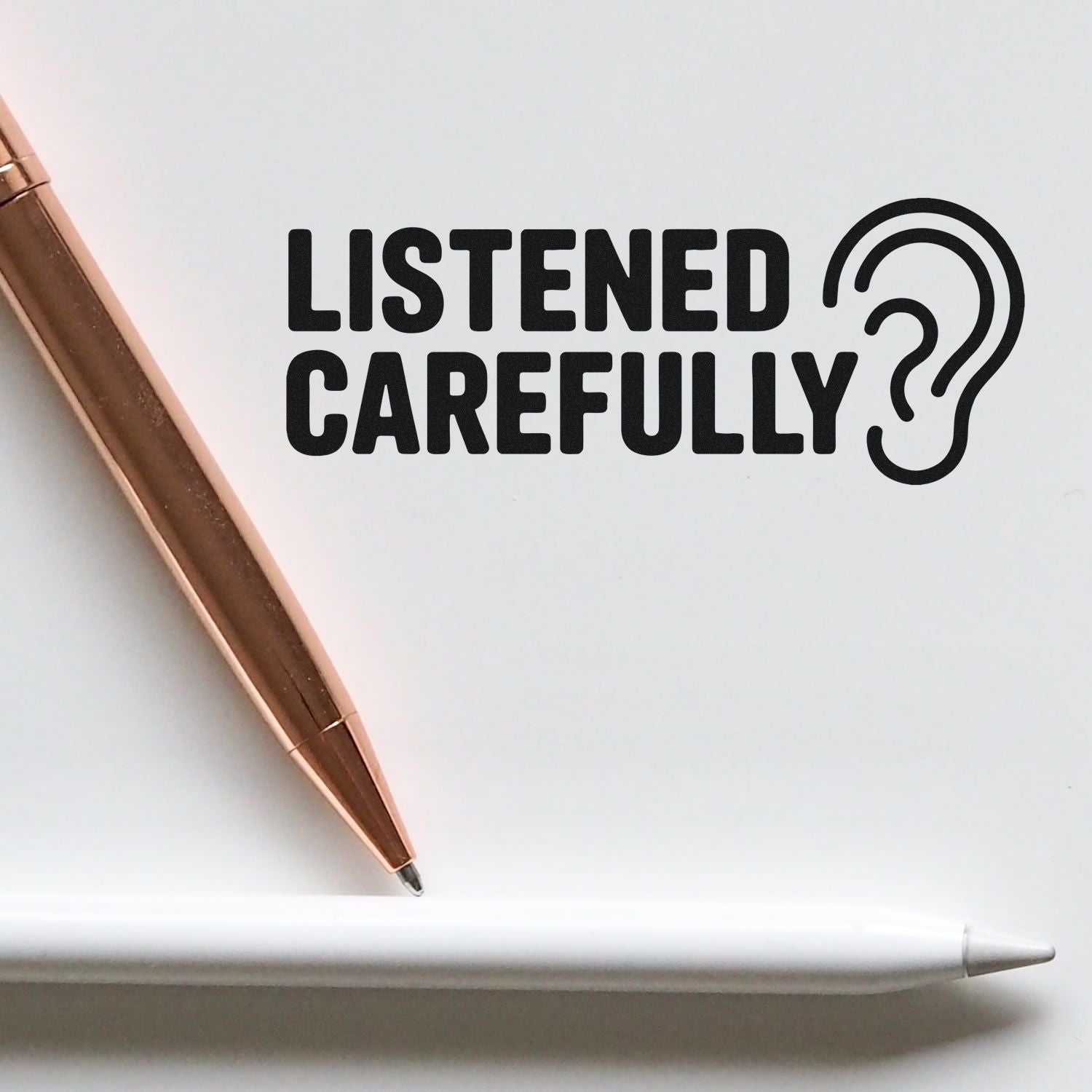 Black LISTENED CAREFULLY stamp with ear icon on white, beside bronze and white seal pens.