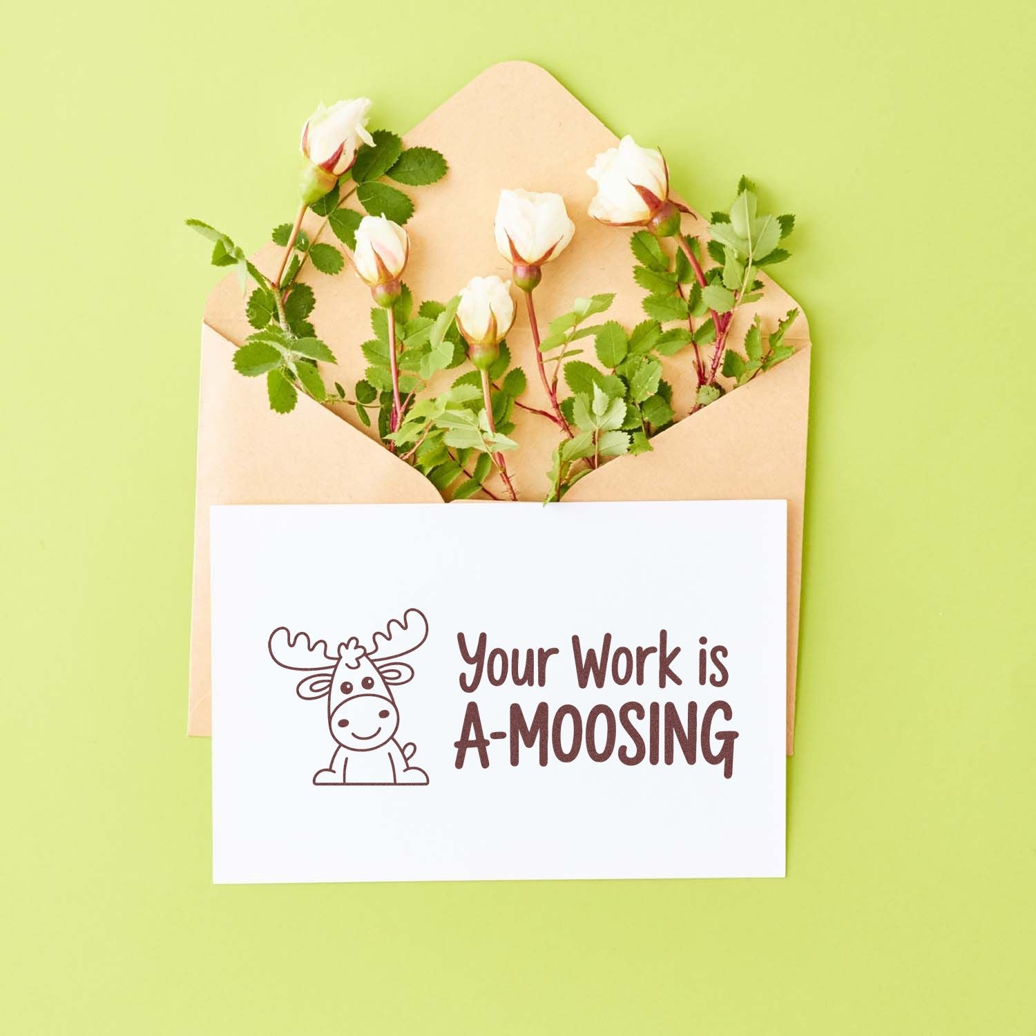 Moose stamp card reading Your Work is A-MOOSING with kraft envelope of white roses on a light green background.