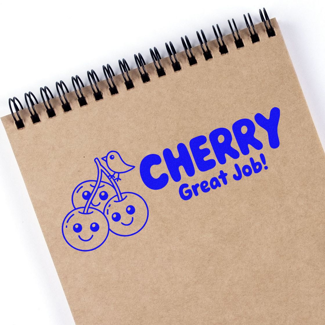 Blue cherry Great Job! rubber stamp on a kraft spiral notebook, with smiling cherries.