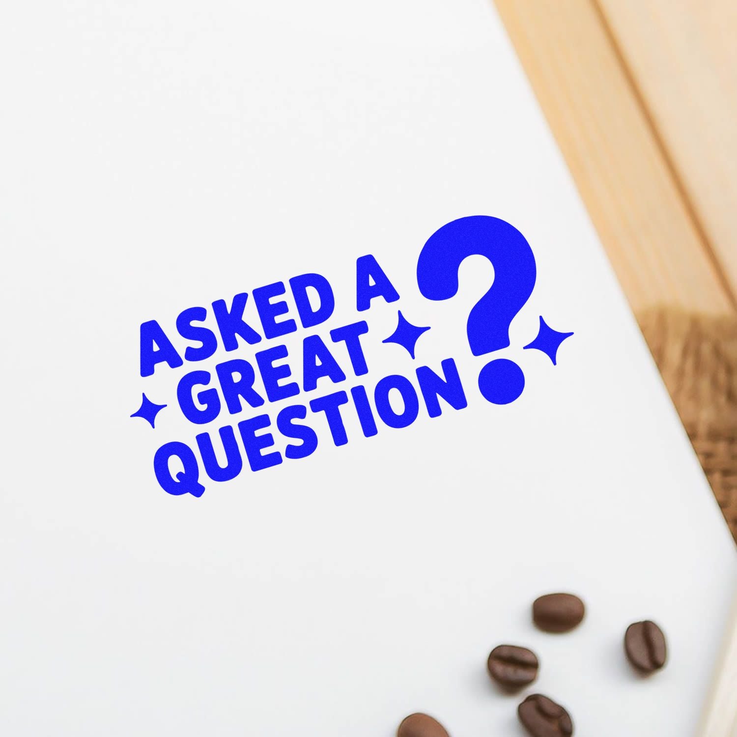 Blue stamp seal reading ASKED A GREAT QUESTION with question mark and sparkles on white paper, coffee beans in corner.