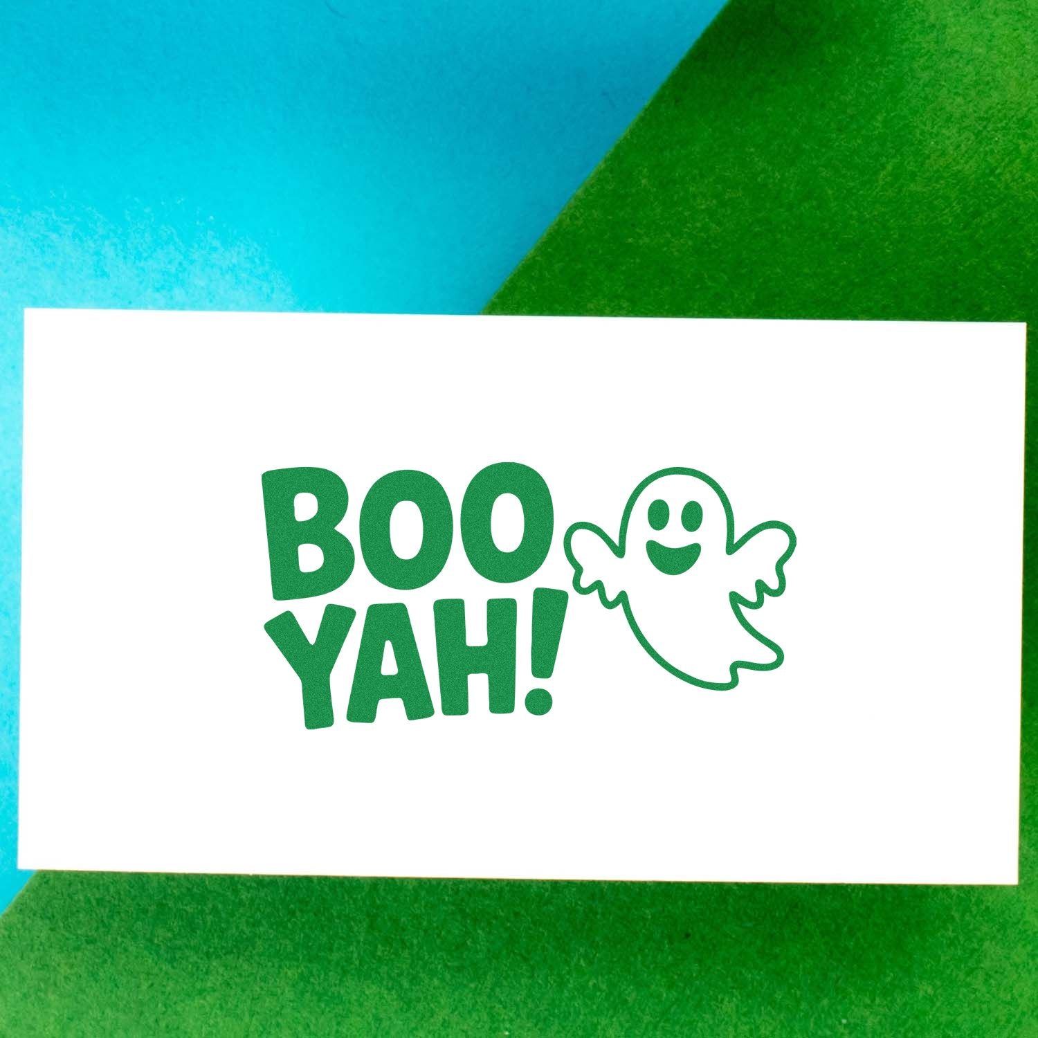 Green BOO YAH! stamp and seal with smiling ghost on white card, set against blue and green background.
