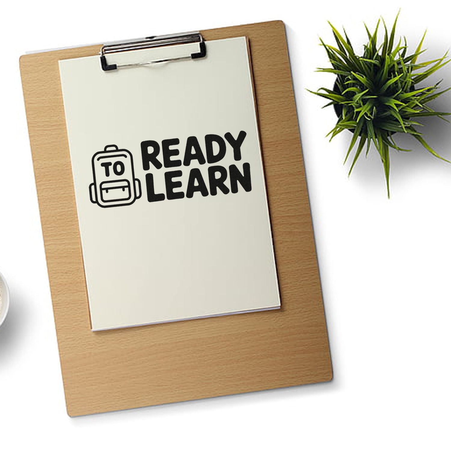 Ready to Learn stamp seal on cream paper clipped to a wooden clipboard, with black backpack icon and green plant.