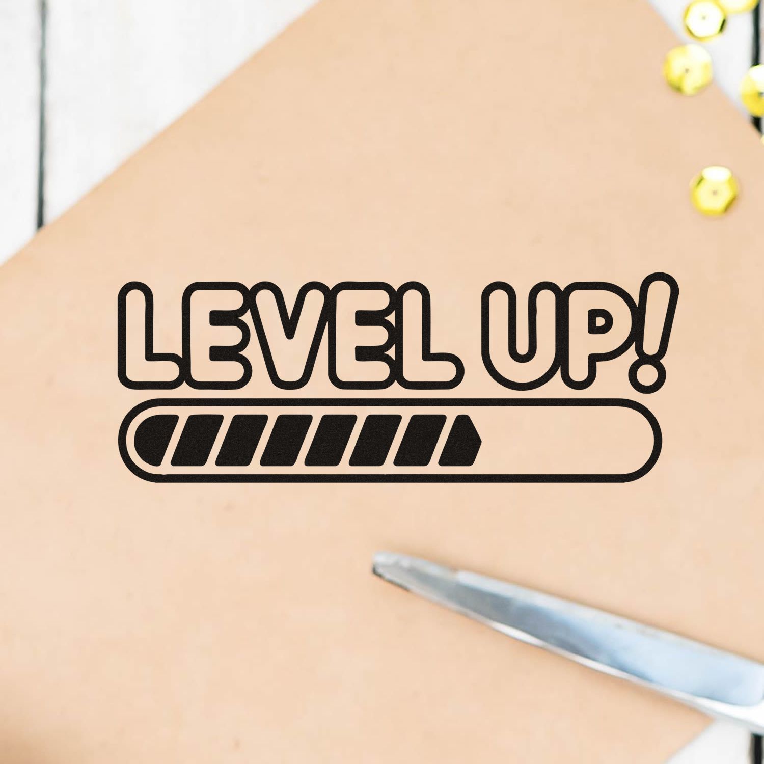 Black LEVEL UP! stamp/seal with progress bar on beige background, accented by yellow gems and a silver craft tool.