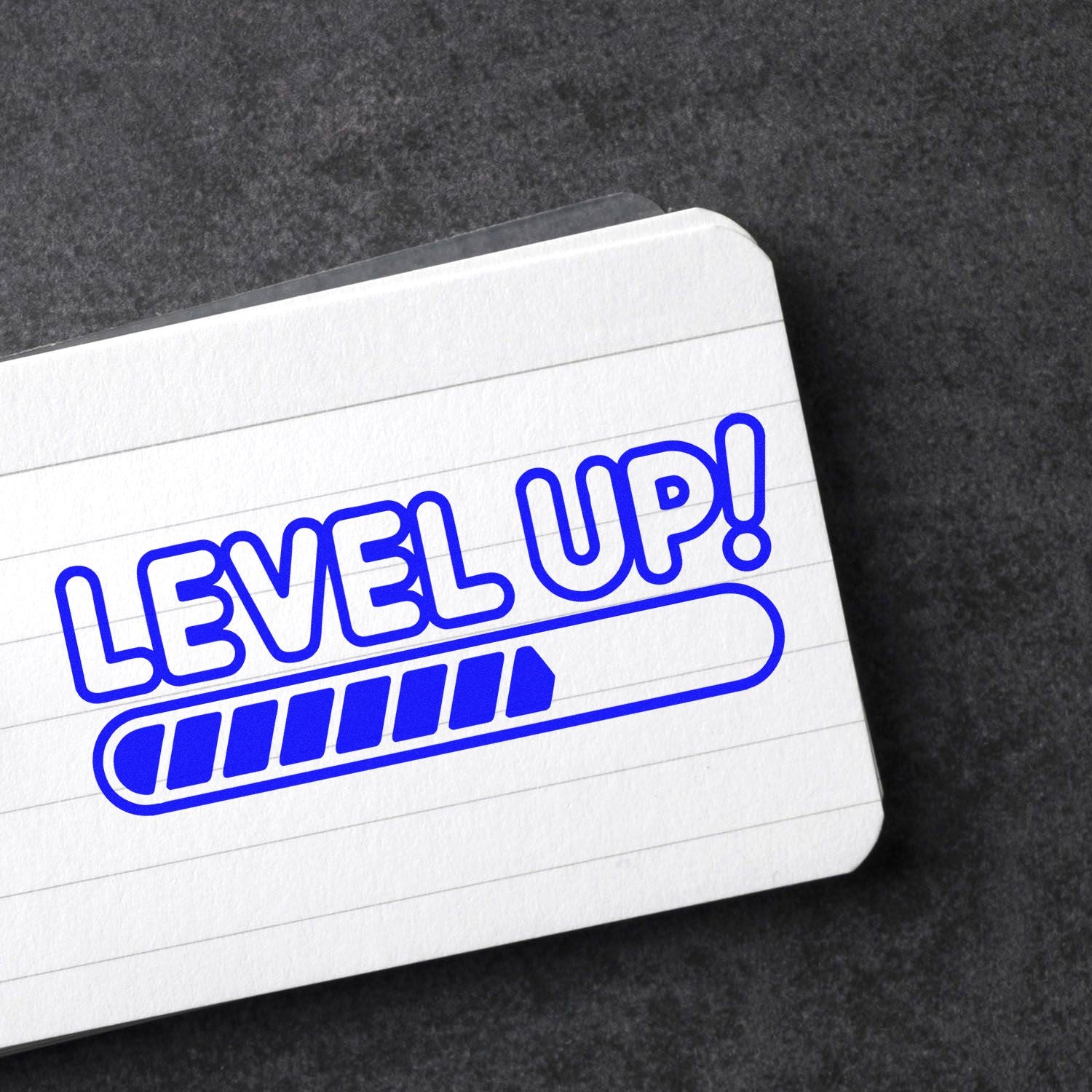 Blue LEVEL UP! stamp and seal with progress bar on a white lined card against a dark background.