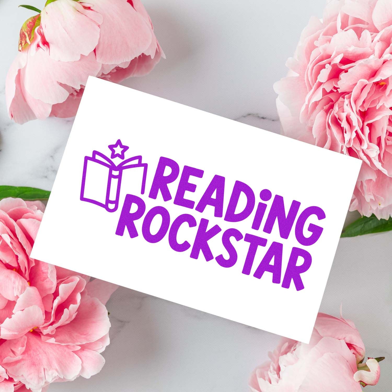 Purple Reading Rockstar stamp and seal with book icon on a white card, surrounded by pink peonies.