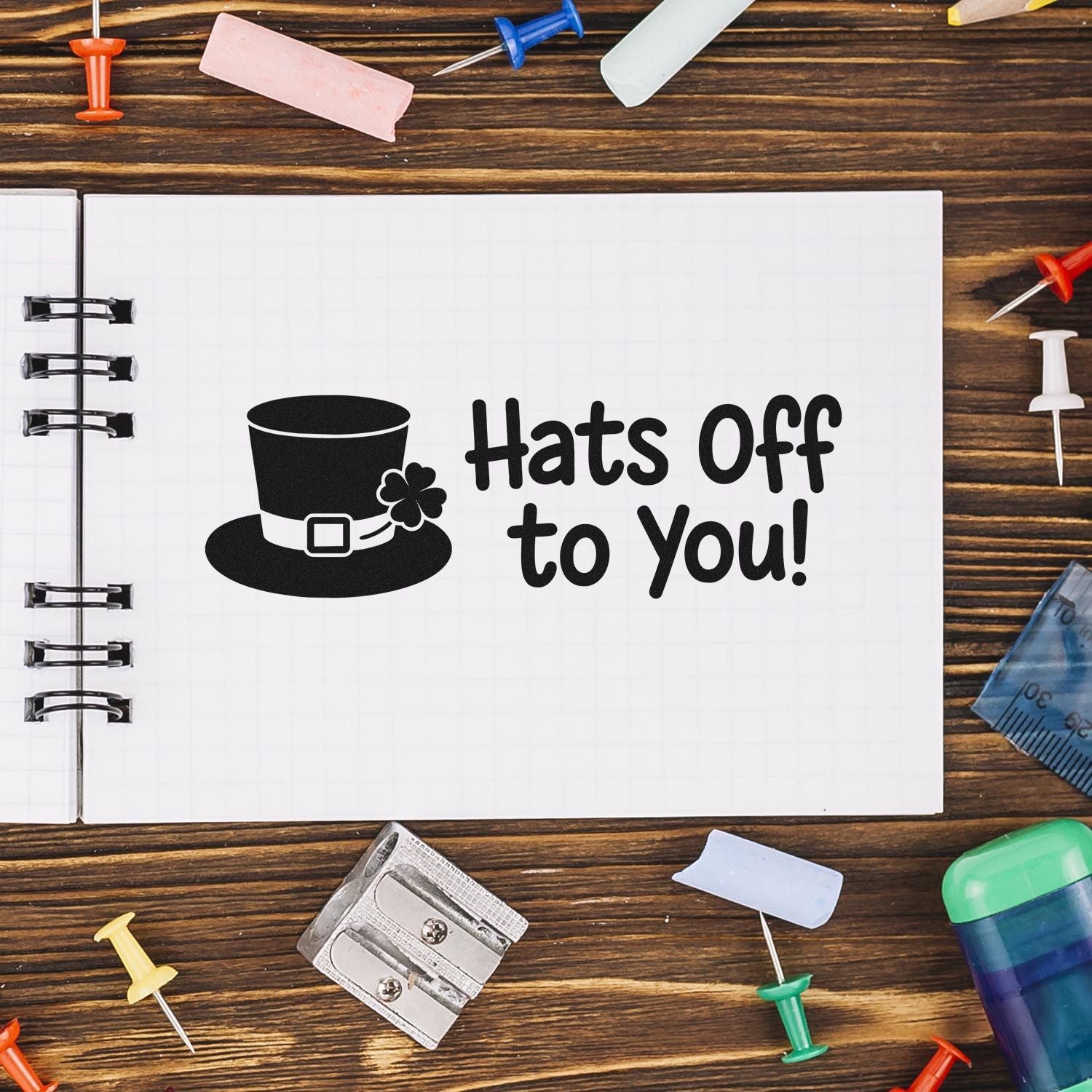 Novelty stamp and seal on a notebook: black top hat with Hats Off to You! on white pages, surrounded by colorful pushpins.