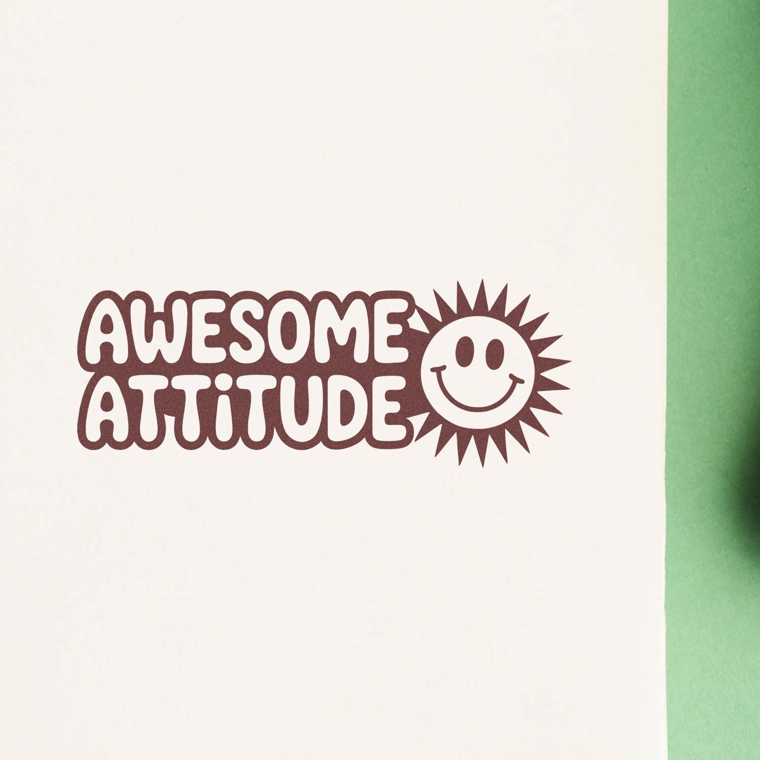 Brown rubber stamp reading AWESOME ATTITUDE with a smiling sun seal on white paper, green edge.