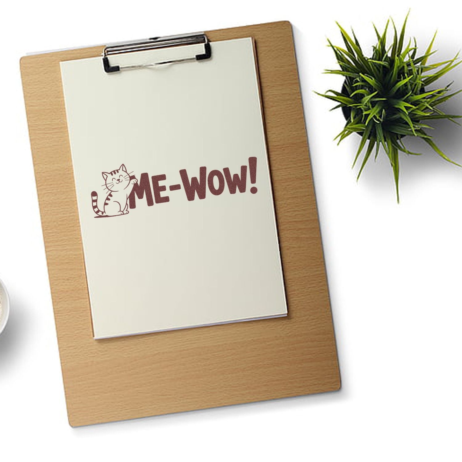 Custom stamp and seal with cat ME-WOW! on white paper clipped to a wooden clipboard, with green plant.