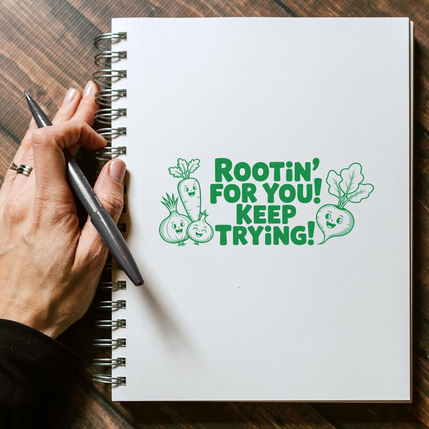 Green stamp and seal with smiling veggies and Rootin for you! Keep trying! on a white spiral notebook.