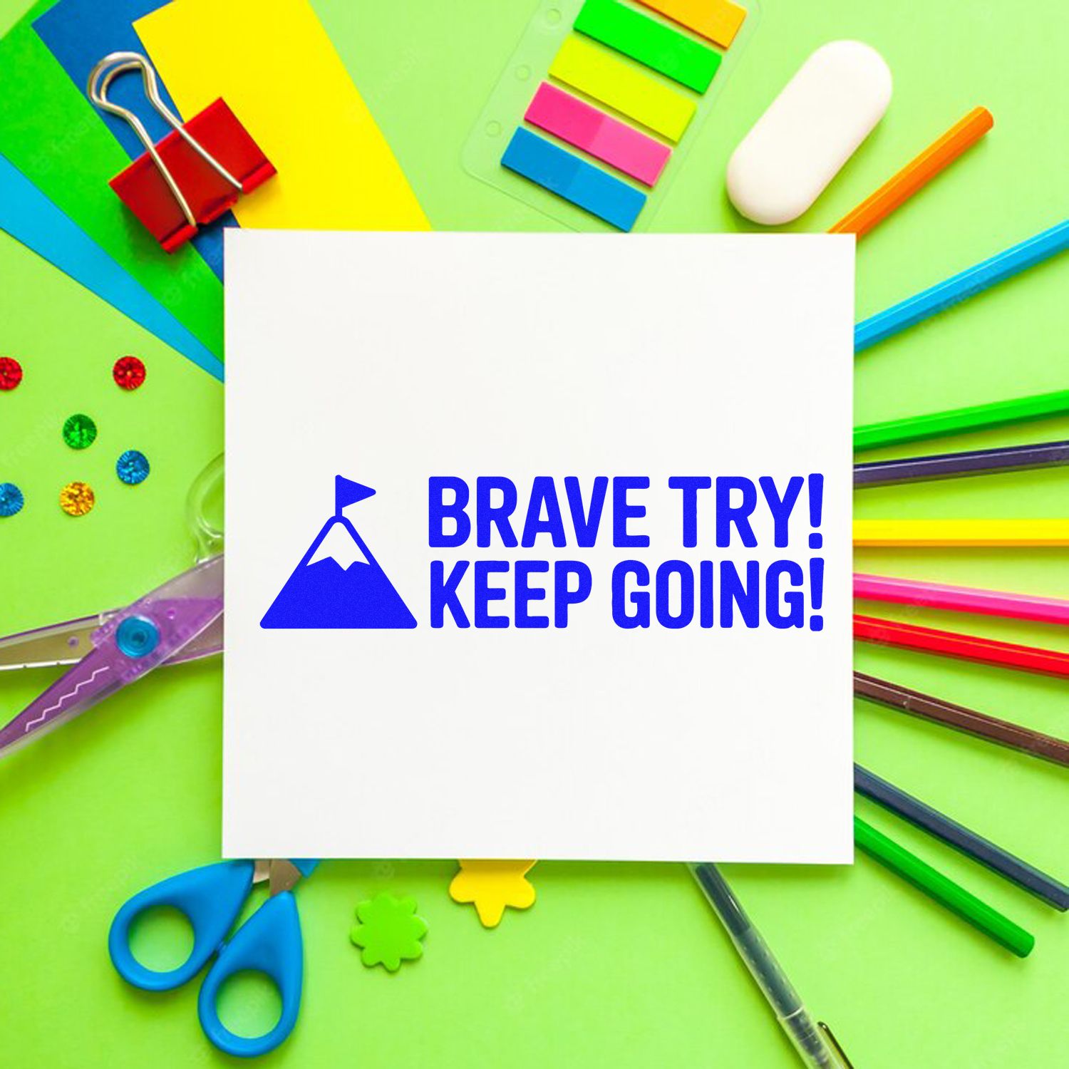 Blue motivational stamp and seal on white card reading BRAVE TRY! KEEP GOING! with colorful stationery on green background.