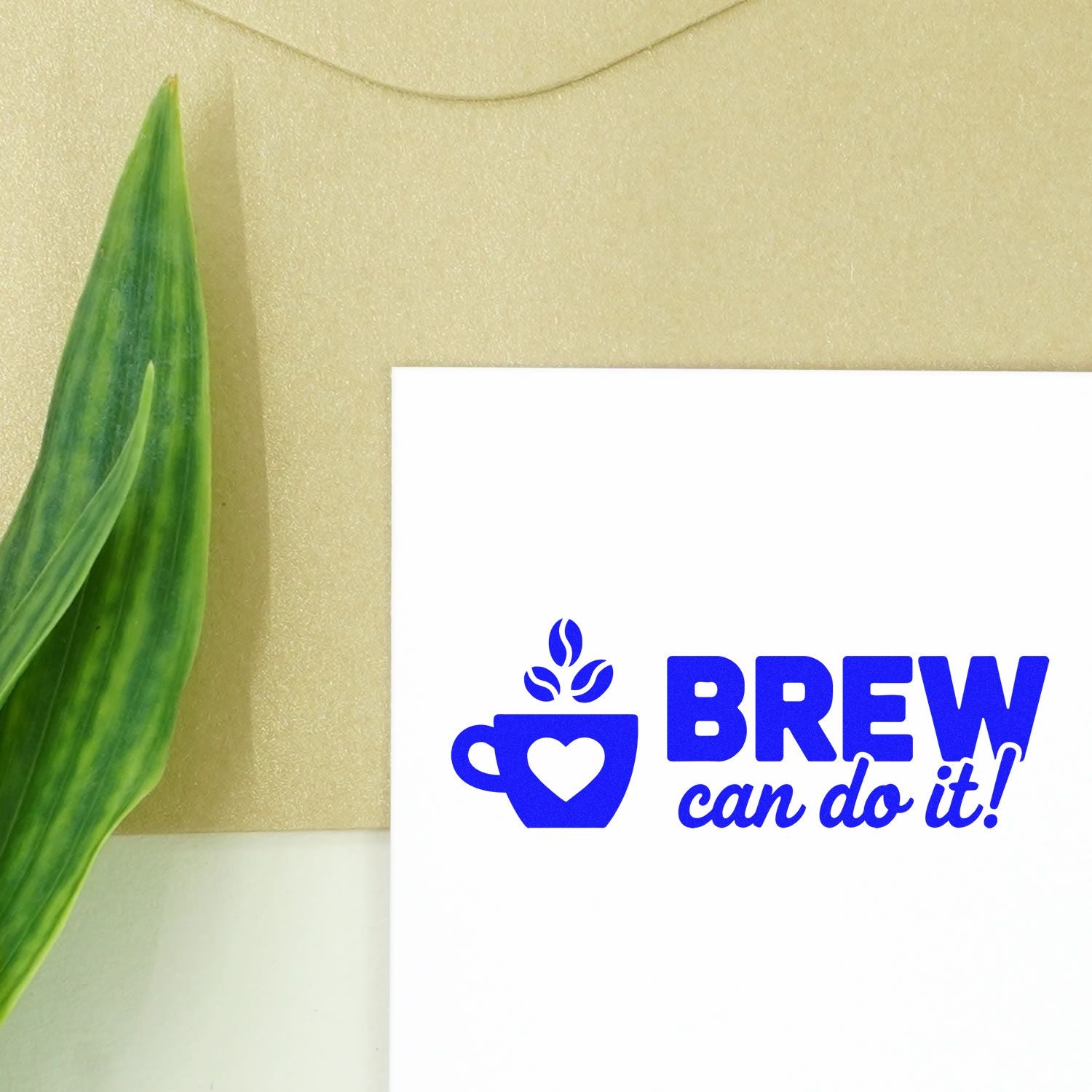 Blue custom stamp and seal with coffee cup logo and BREW can do it! on white paper, beside a green leaf on beige background.