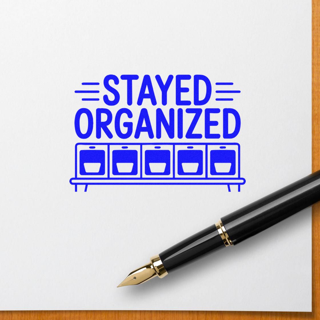 Blue Stayed Organized stamp with storage bins on white paper, beside a black fountain pen with gold nib.