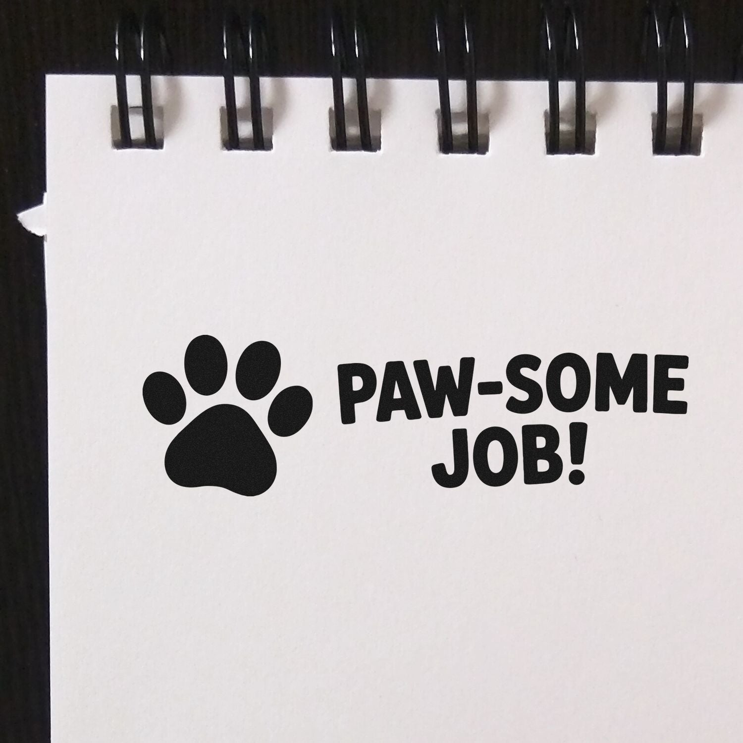 Black paw print stamp seal with PAW-SOME JOB! on a white spiral-bound page
