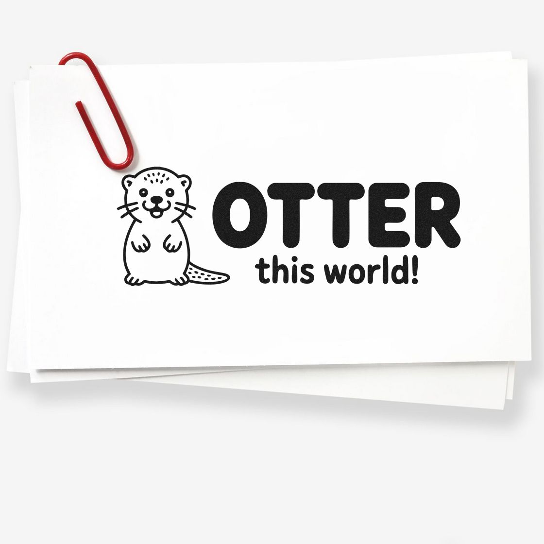 Custom stamp/seal design with black otter and OTTER this world! on white card, accented by a red paperclip.