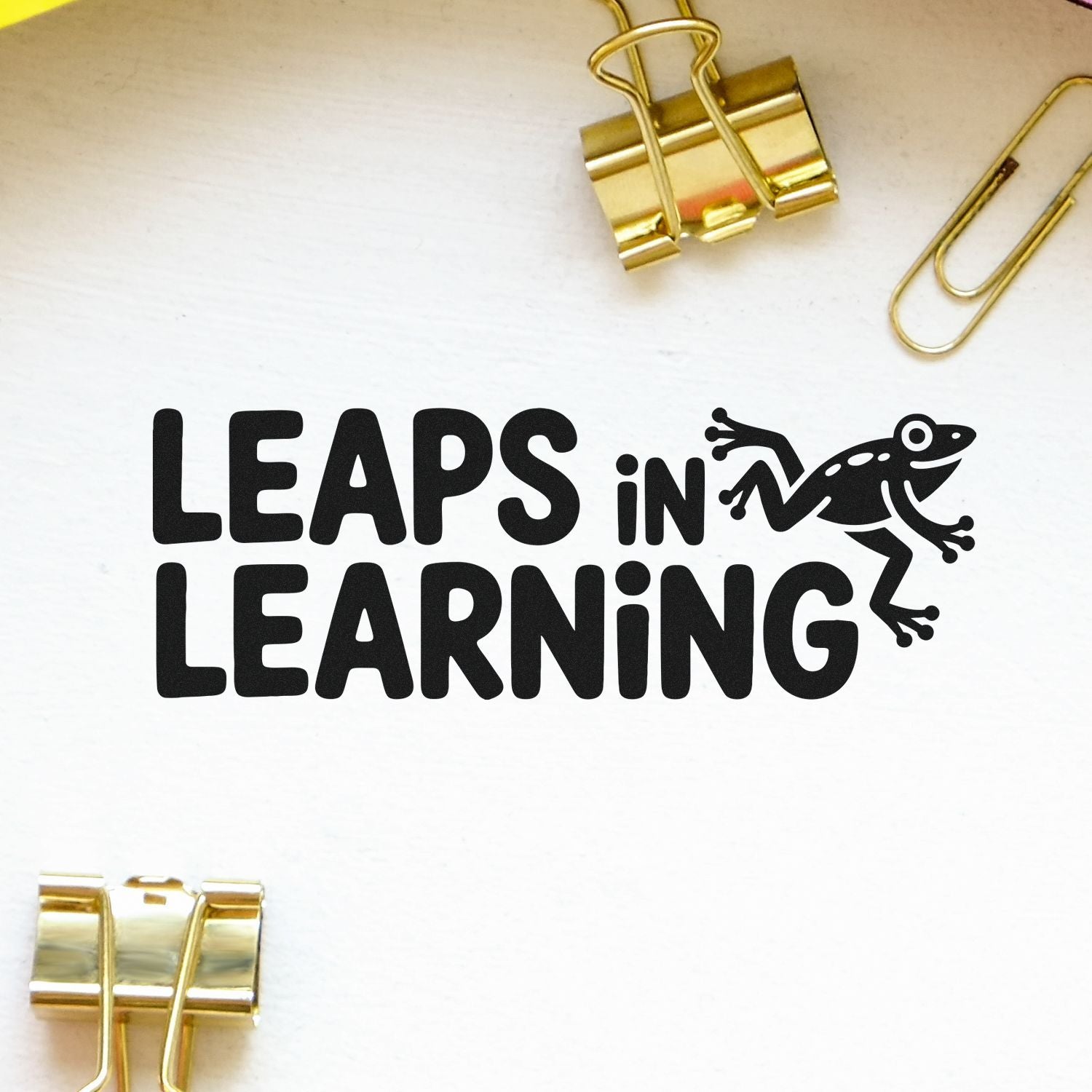 Black Leaps in Learning stamp and seal with frog icon on white background, accented by gold binder clips.