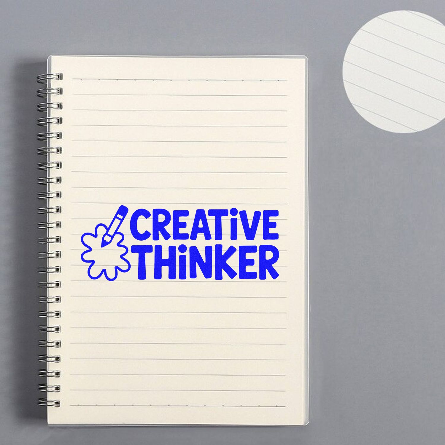 Blue Creative Thinker stamp with pencil icon on lined spiral notebook, gray background, matching paper seal at top right.