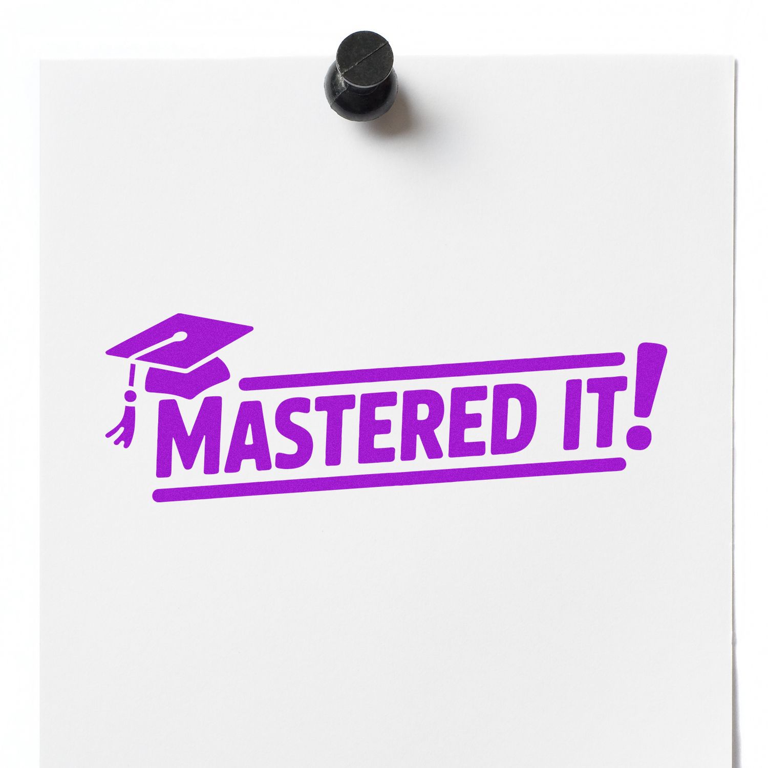Black rubber seal stamp on white paper, printing purple MASTERED IT! with graduation cap icon.